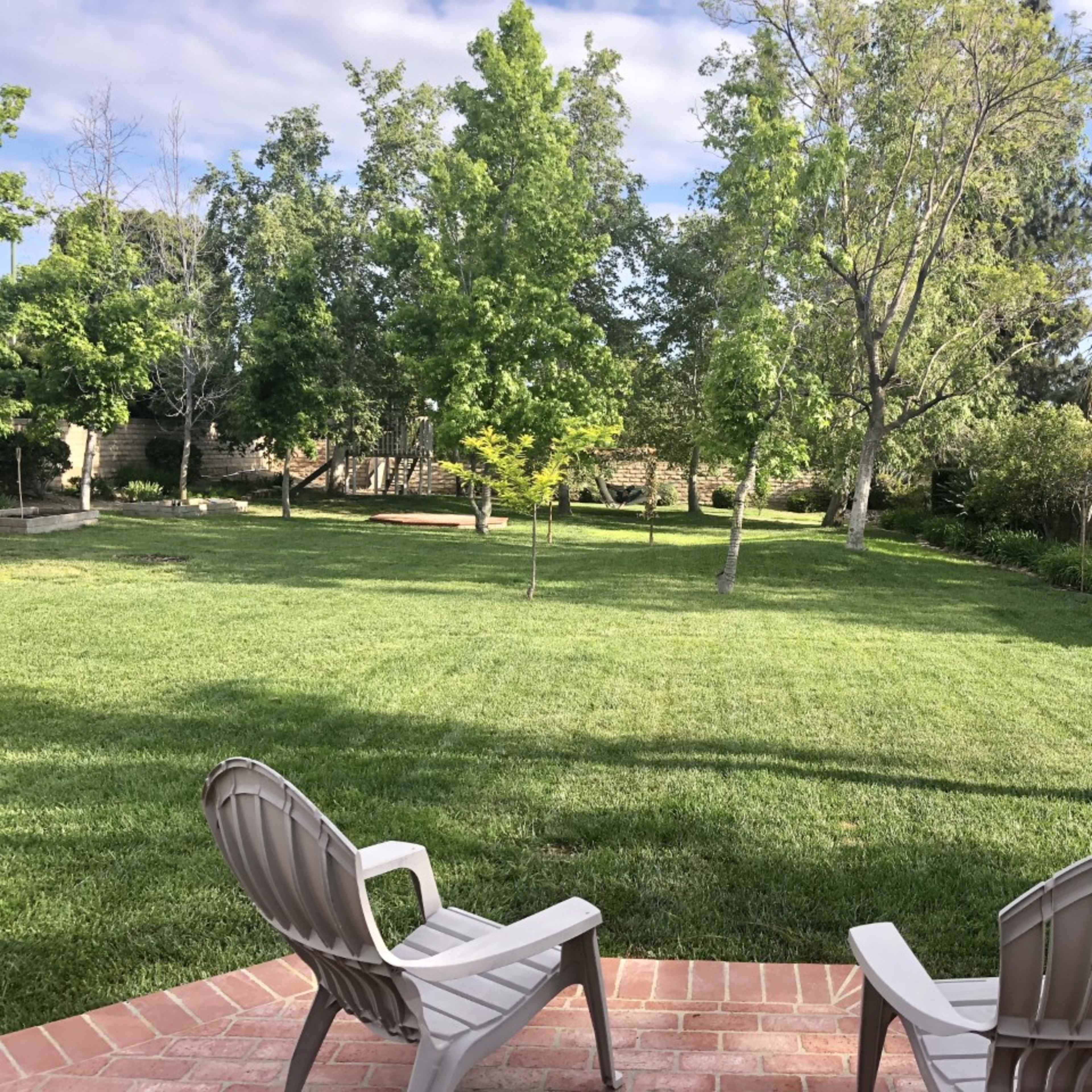 A pair of lawn chairs sits on a brick patio overlooking a green grassy area surrounded by trees.