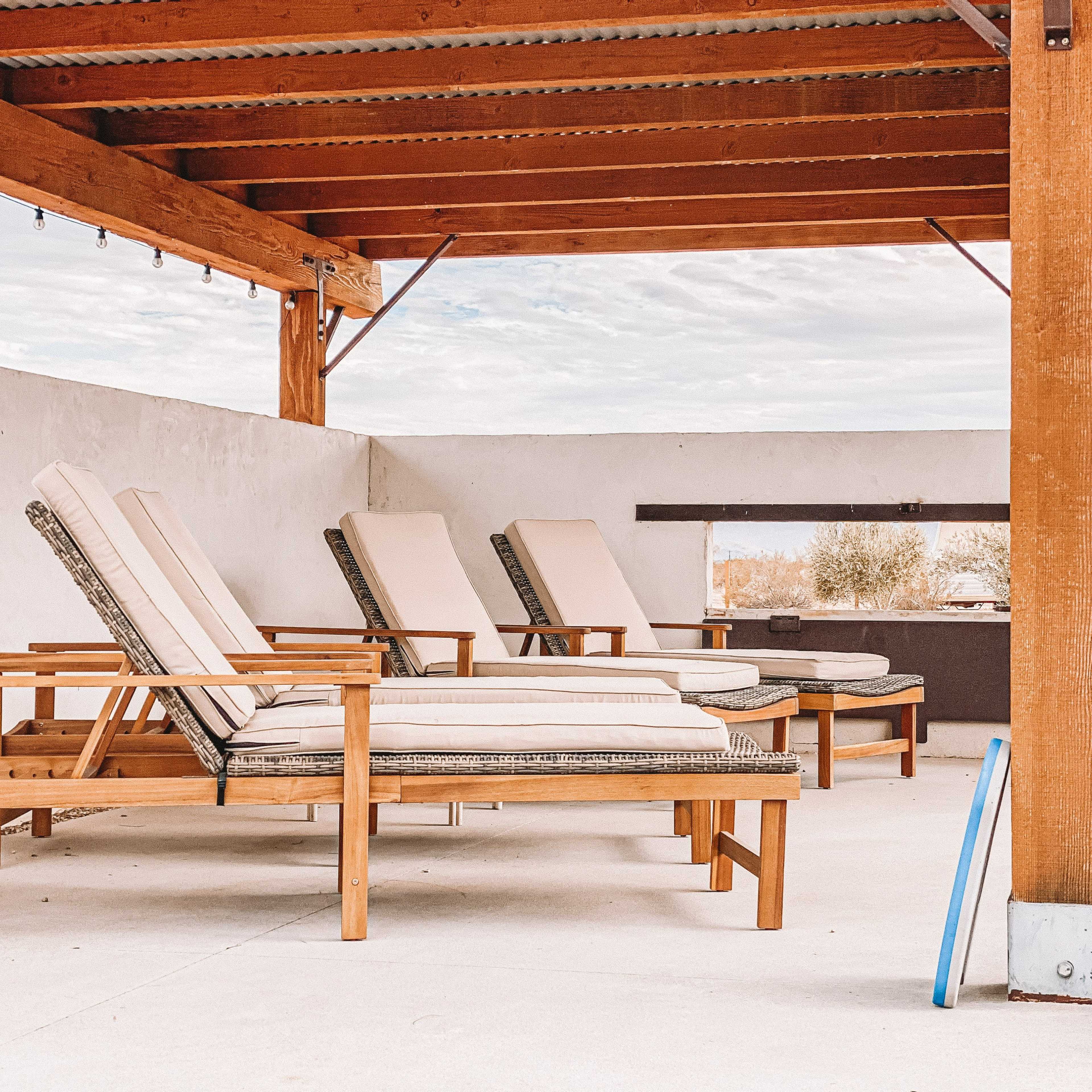 Several wooden lounge chairs with light-colored cushions arranged under a wooden pergola.