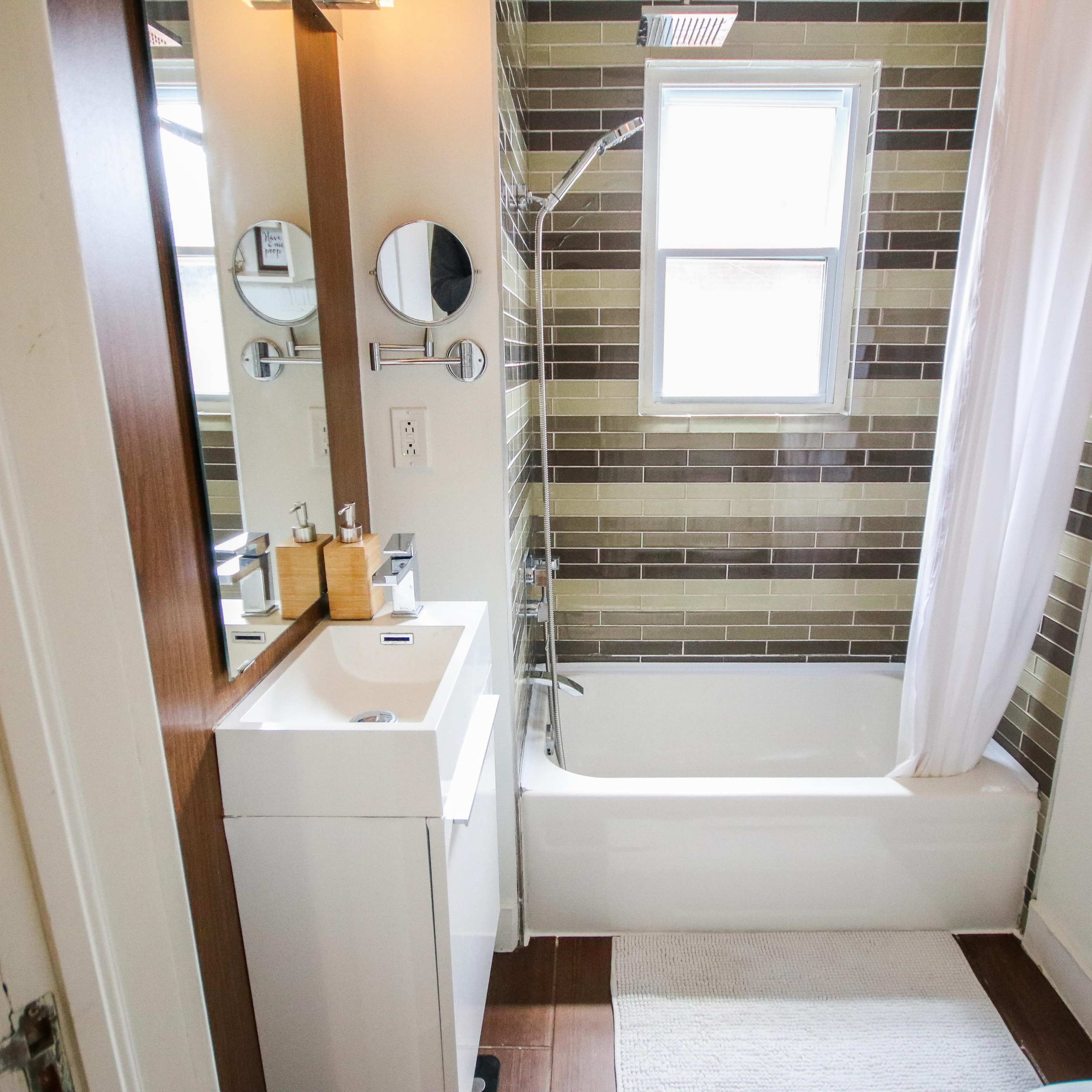 A modern bathroom featuring a bathtub with a shower, a vanity with a mirror, and a window allowing natural light.