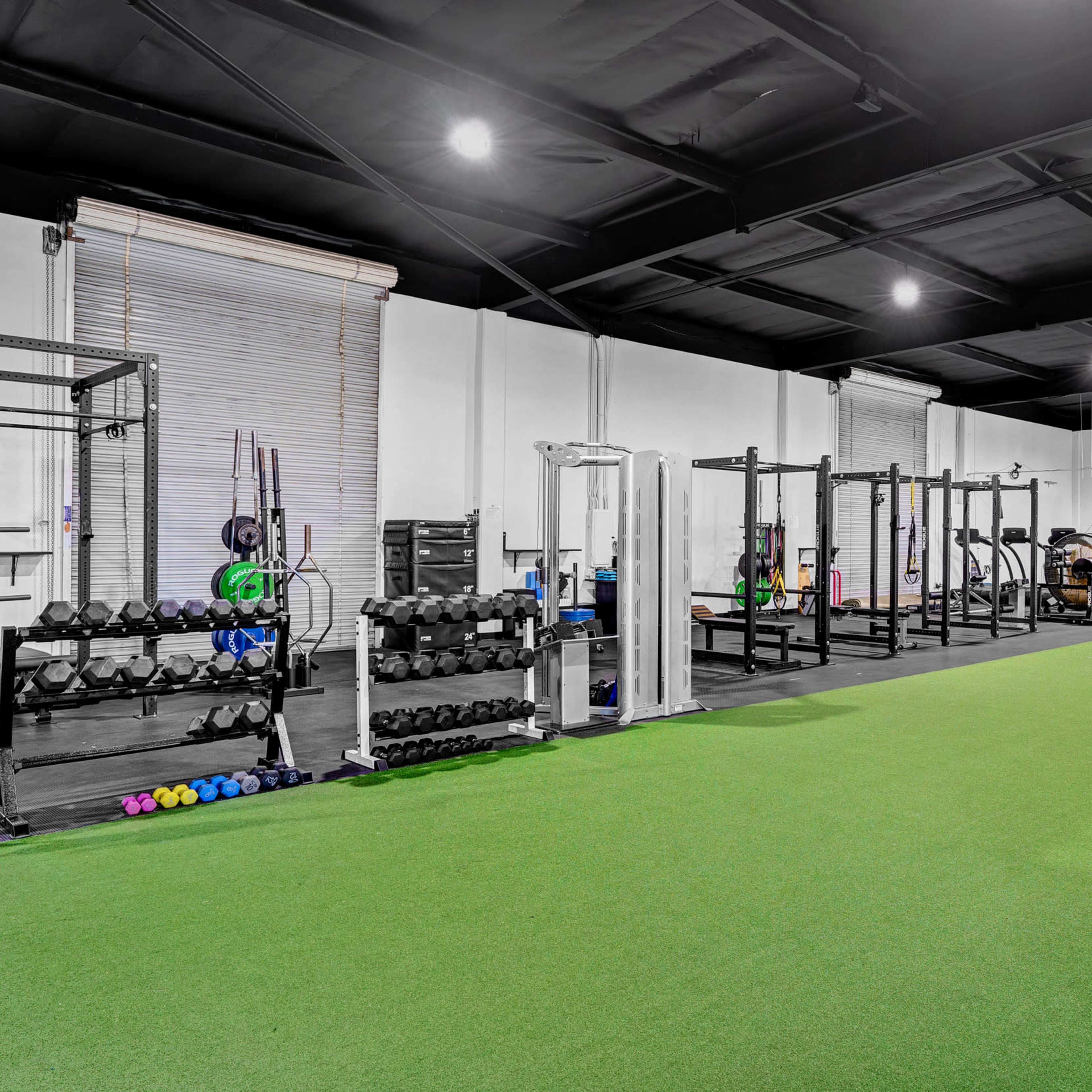 A gym interior with a green turf area, weightlifting equipment, and a wall featuring the name "NOVOS."