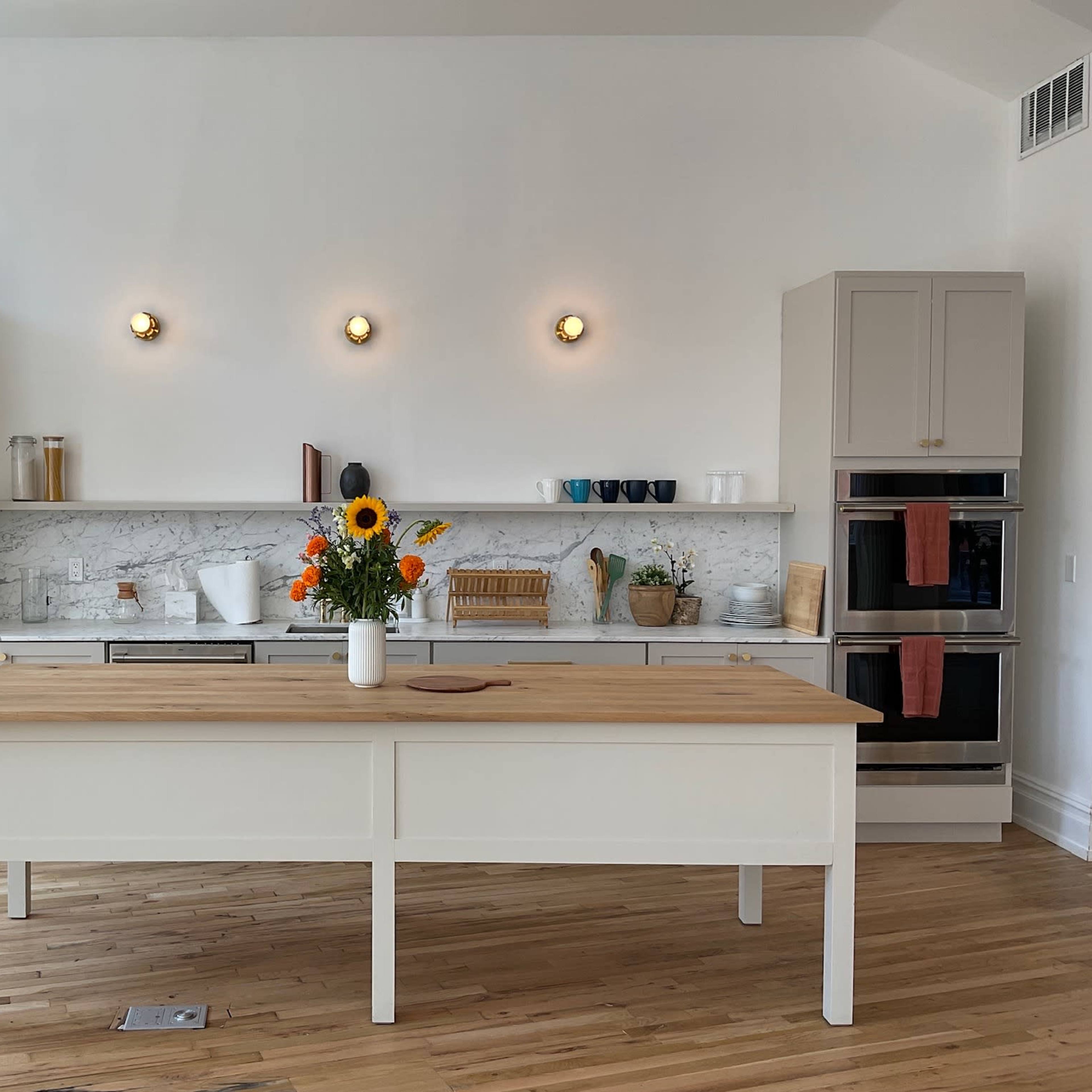 A modern kitchen features a central wooden island, stainless steel appliances, marble countertops, and a vase of sunflowers.