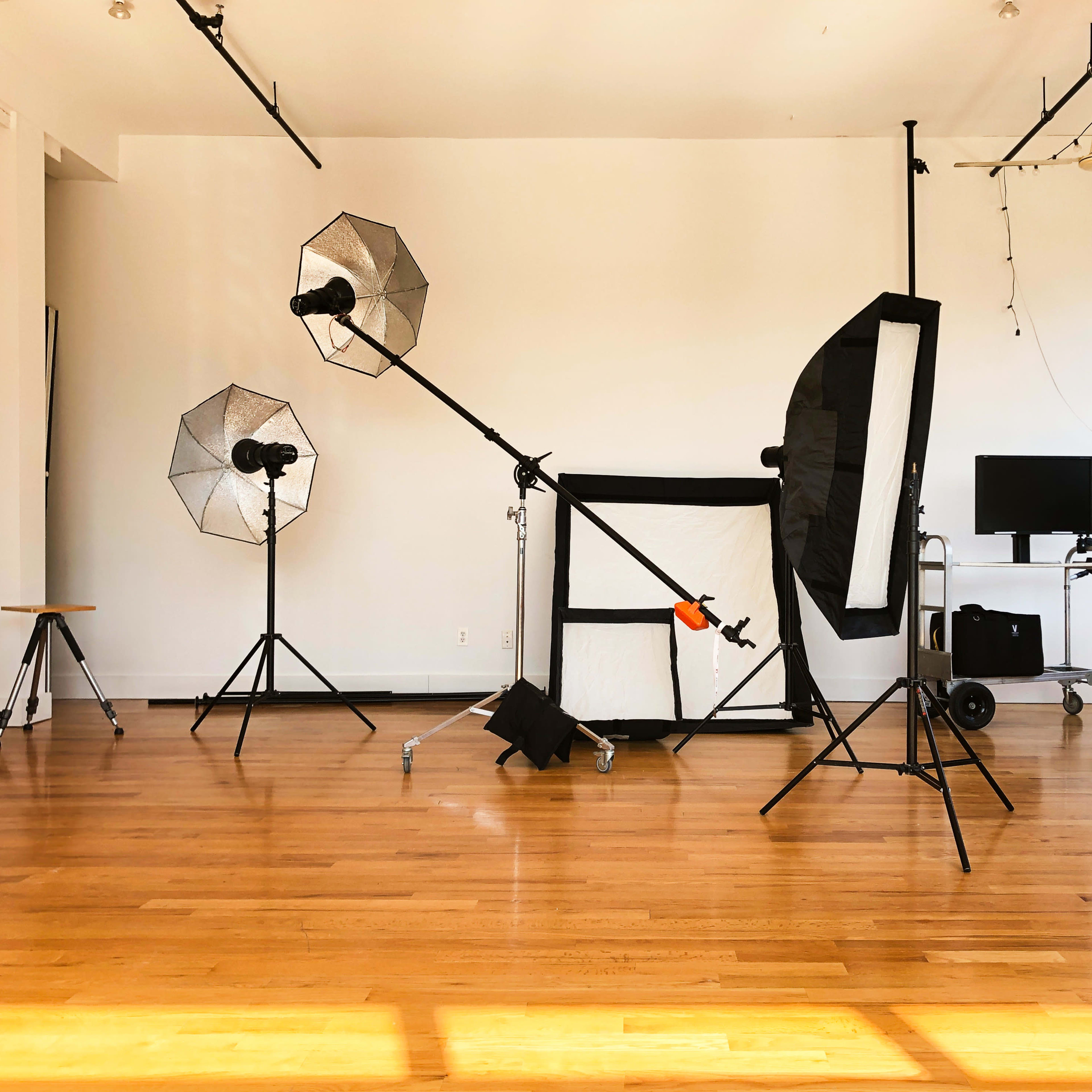 A photography studio features several lighting rigs, a backdrop, and various equipment arranged on a wooden floor.