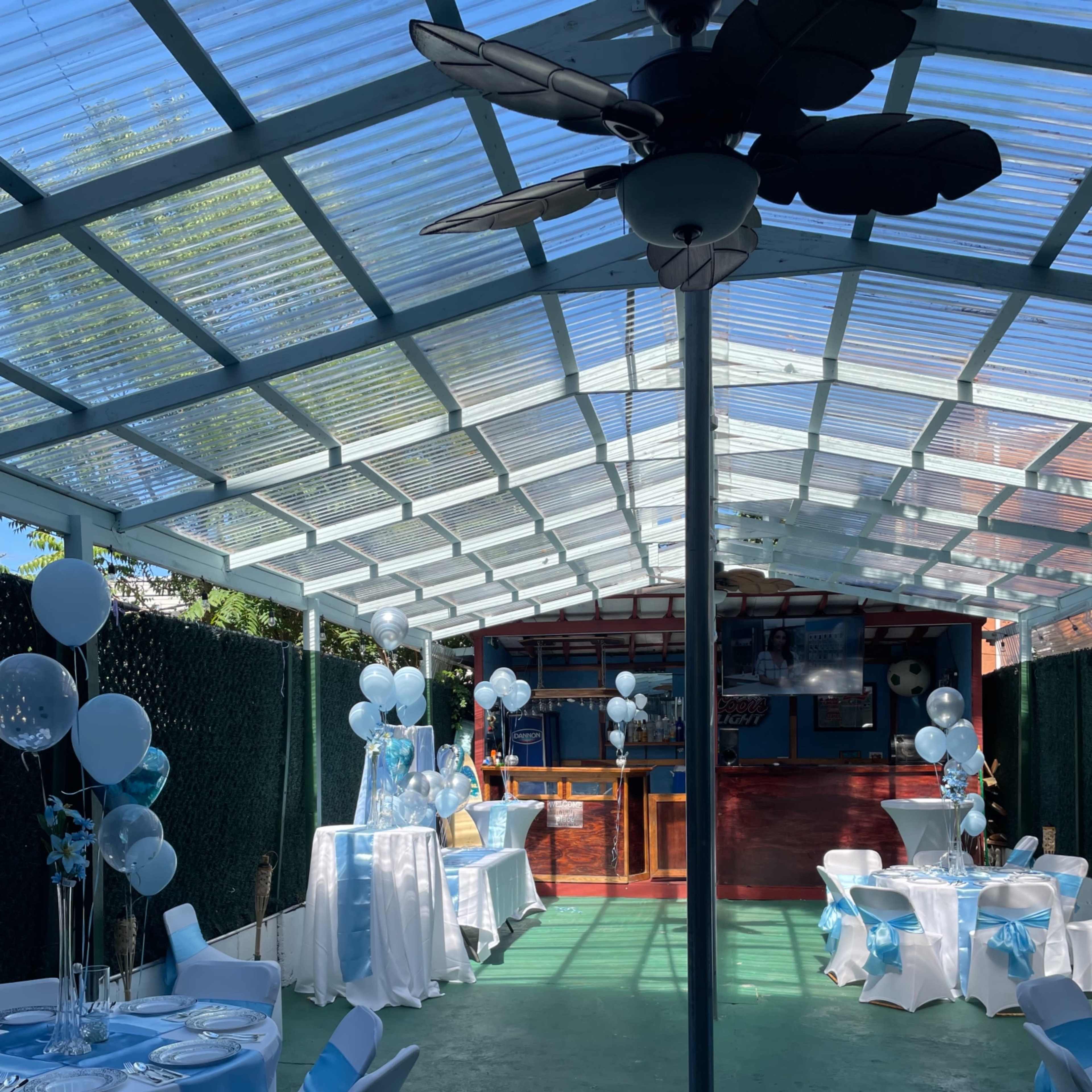 An outdoor party space with decorated tables and balloons arranged in a canopy-covered area.