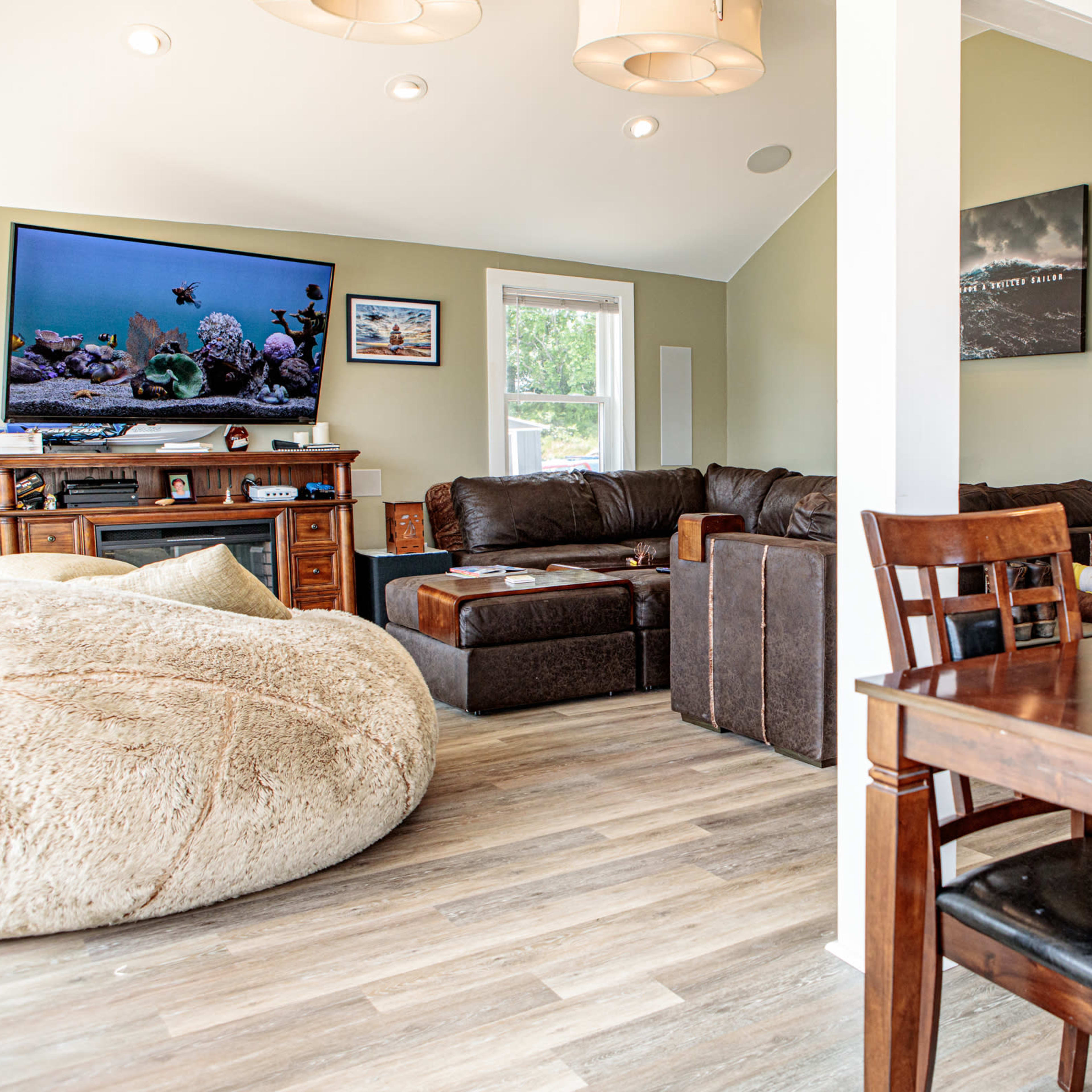 A cozy living area featuring a large bean bag chair, a television mounted on the wall, and a dining table with wooden chairs.