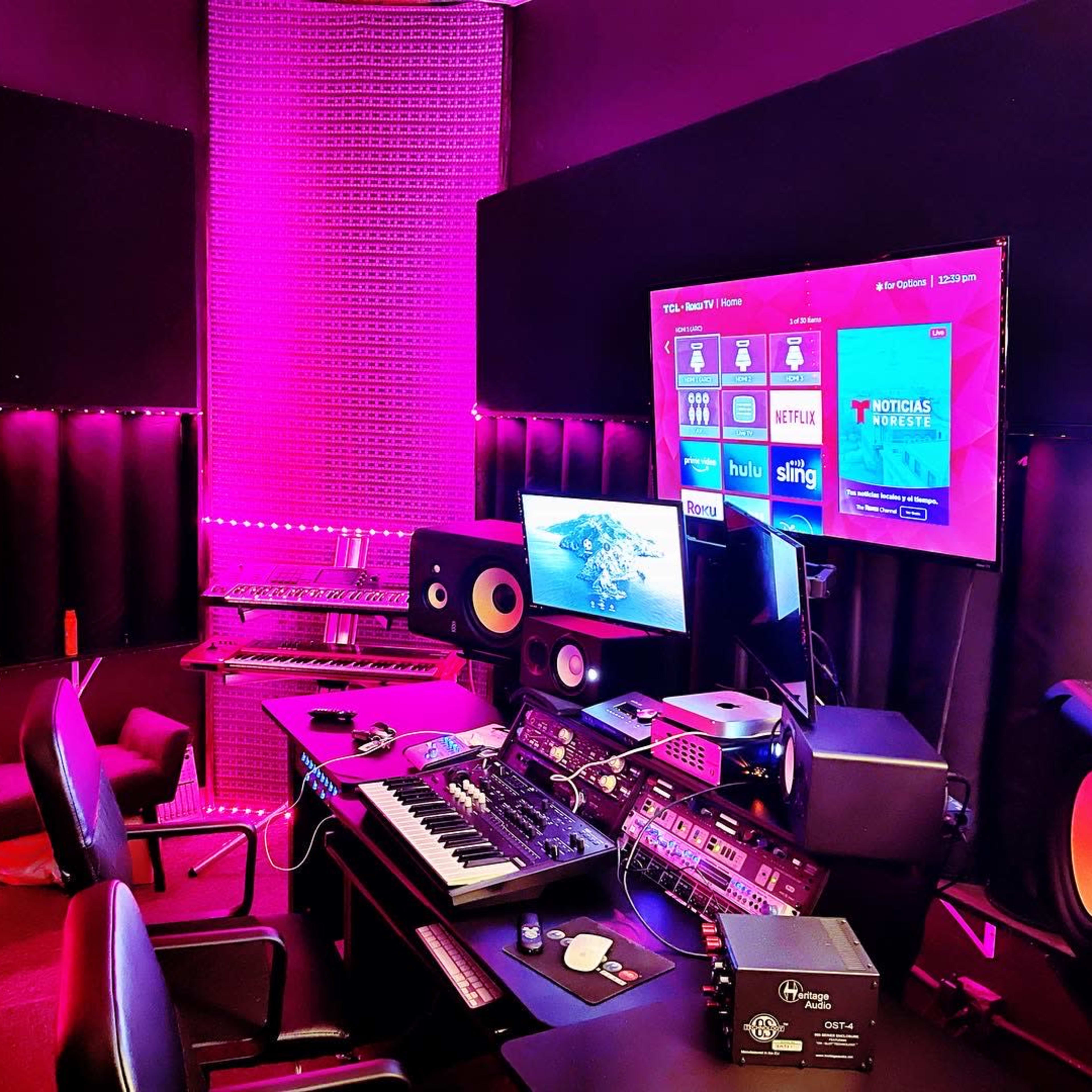 A music studio is equipped with a keyboard, multiple monitors, and sound equipment, featuring purple ambient lighting.