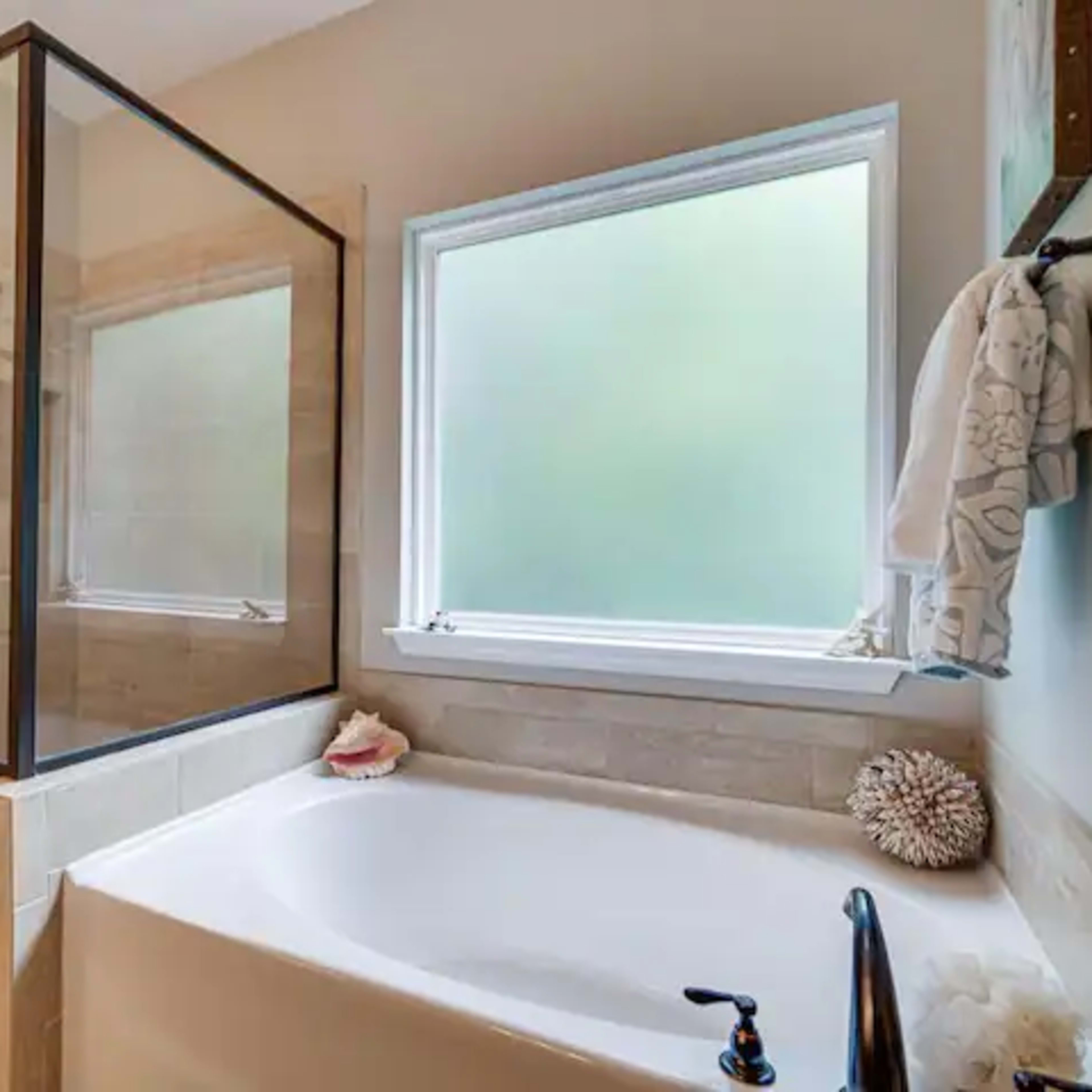 A modern bathroom featuring a glass-enclosed shower, a white bathtub, and a window providing natural light.