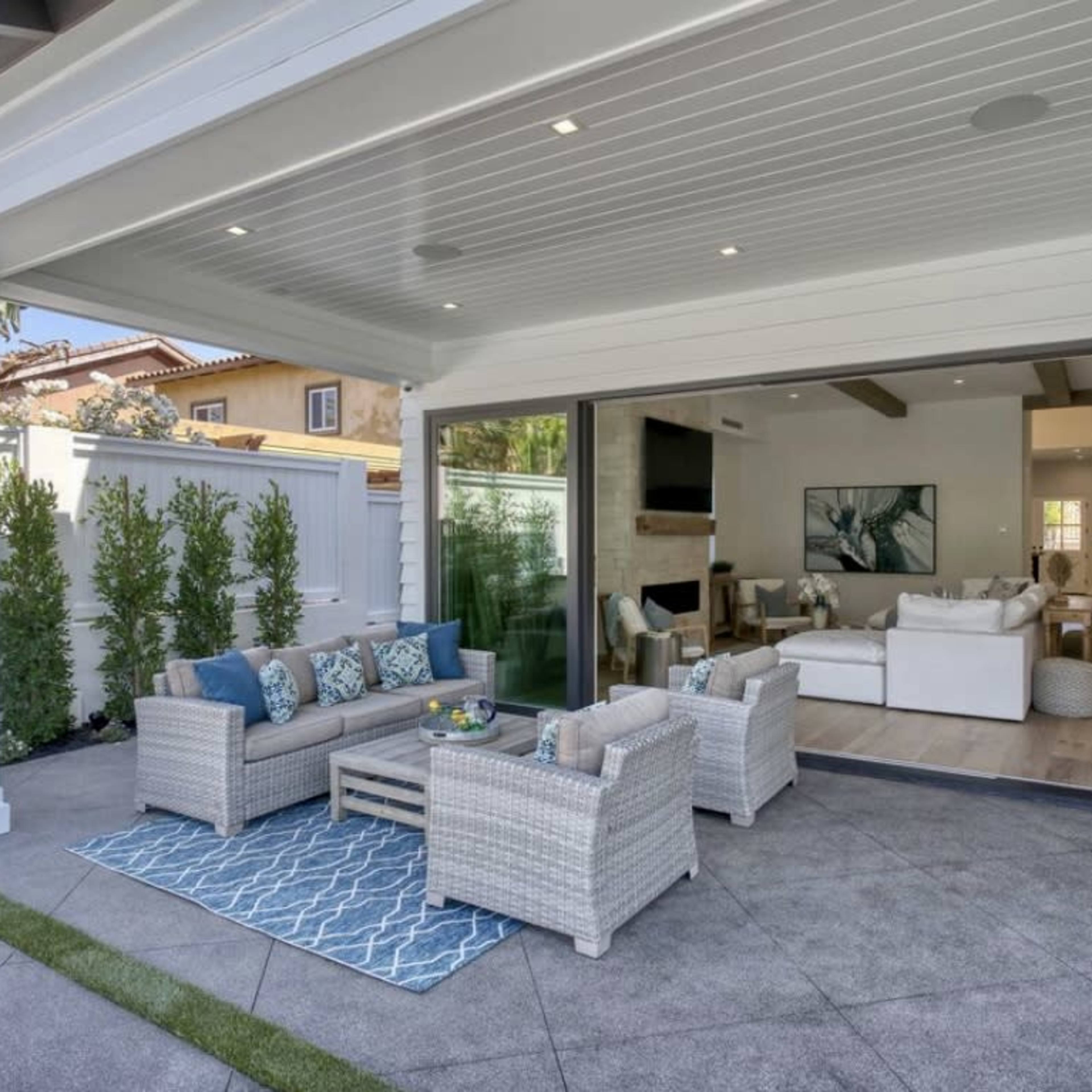 A modern outdoor living area features a wicker seating arrangement on a patterned rug, with a view into a bright and spacious interior.
