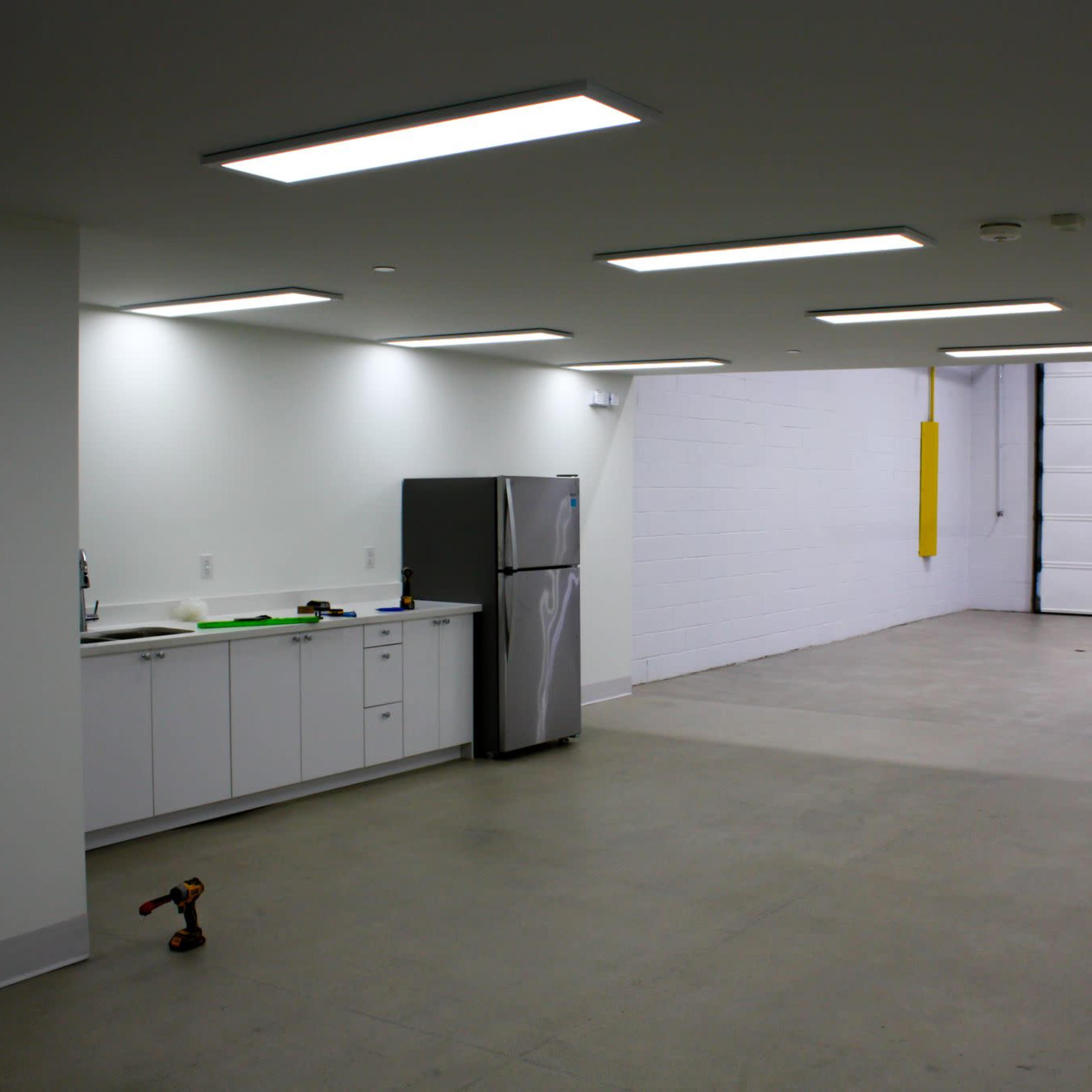 A spacious, empty garage with a kitchenette area on one side and a large roll-up door at the far end.