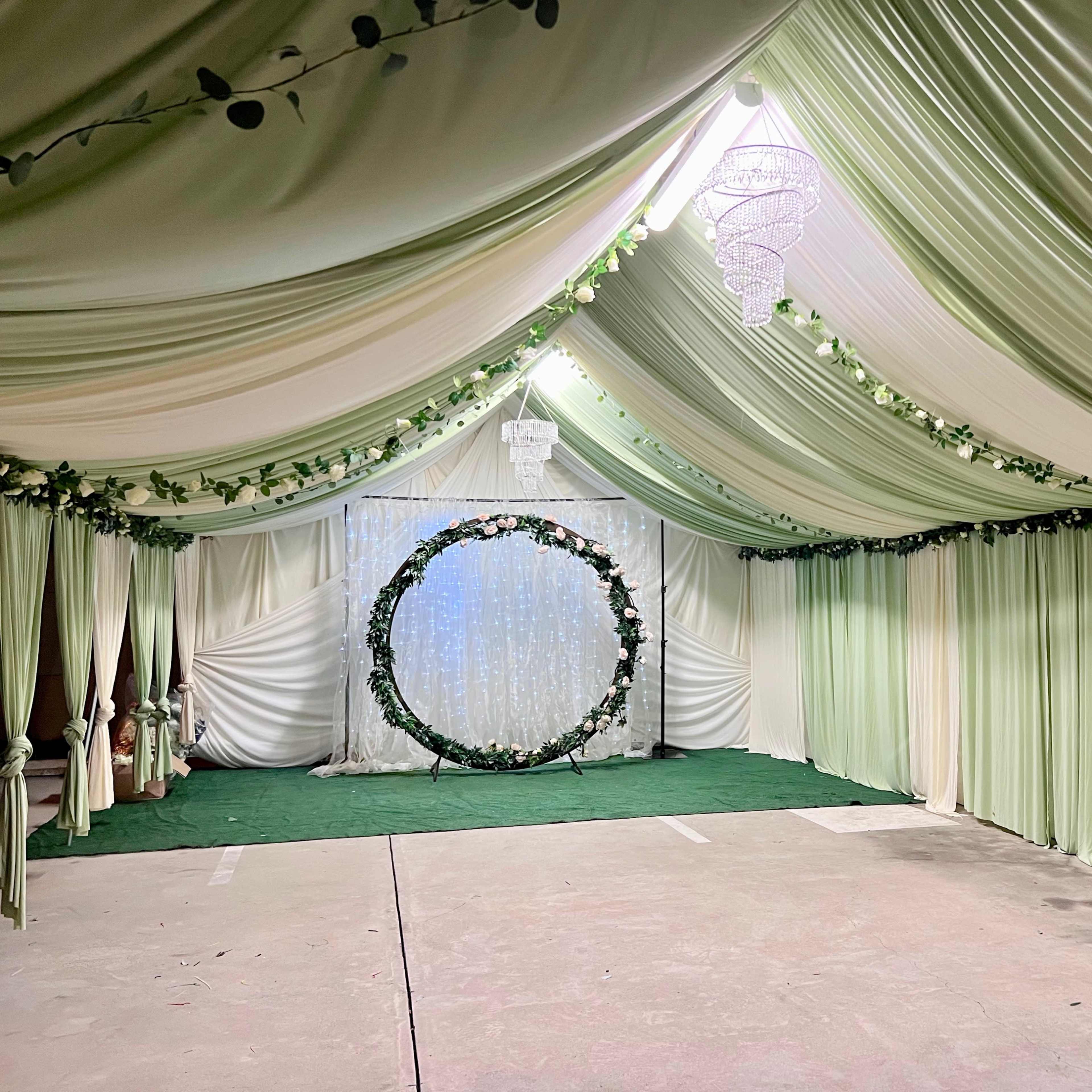 An indoor venue decorated with green and white drapes, featuring a floral circular backdrop at the far end.