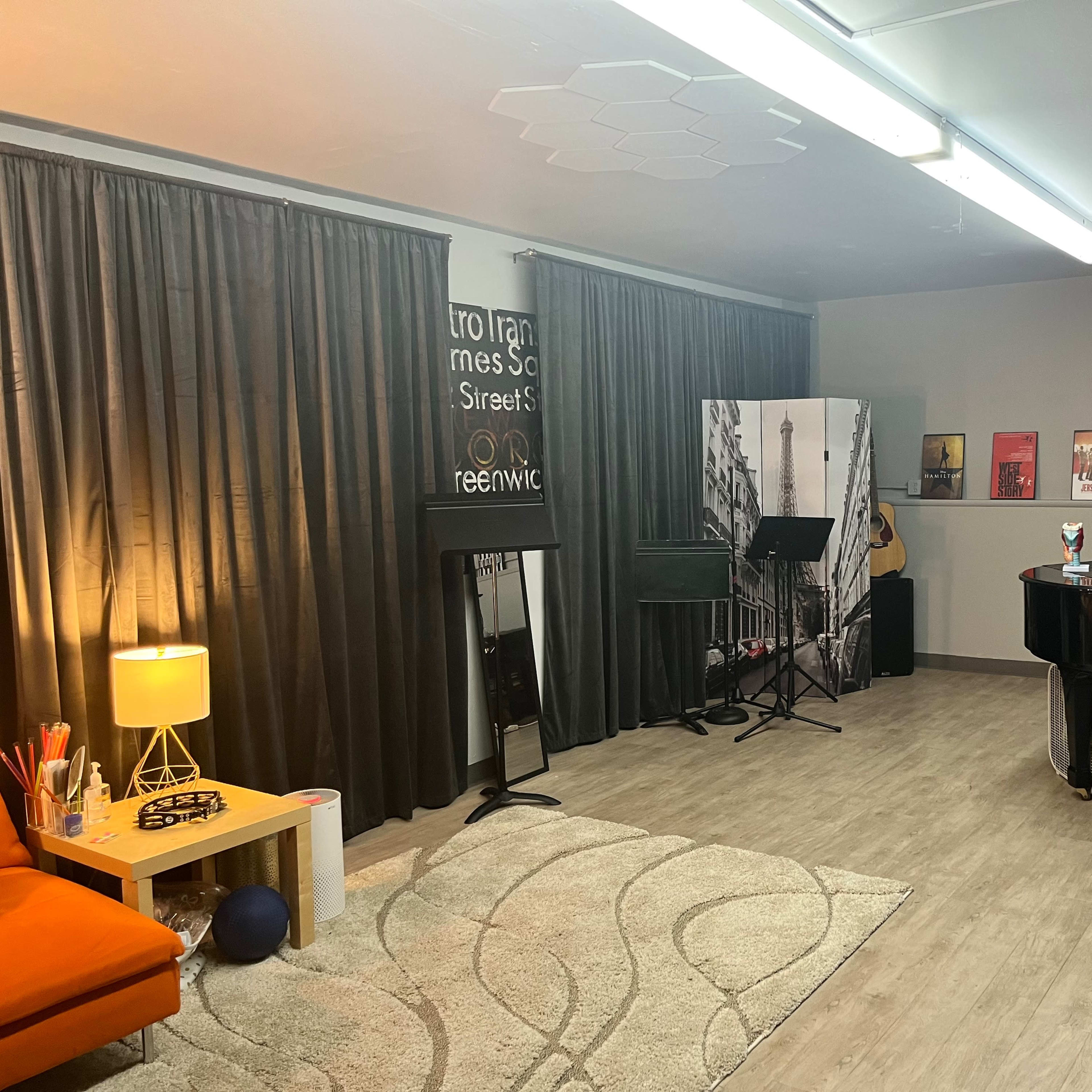 A spacious music studio with a grand piano, a mirrored wall, and various music posters displayed.