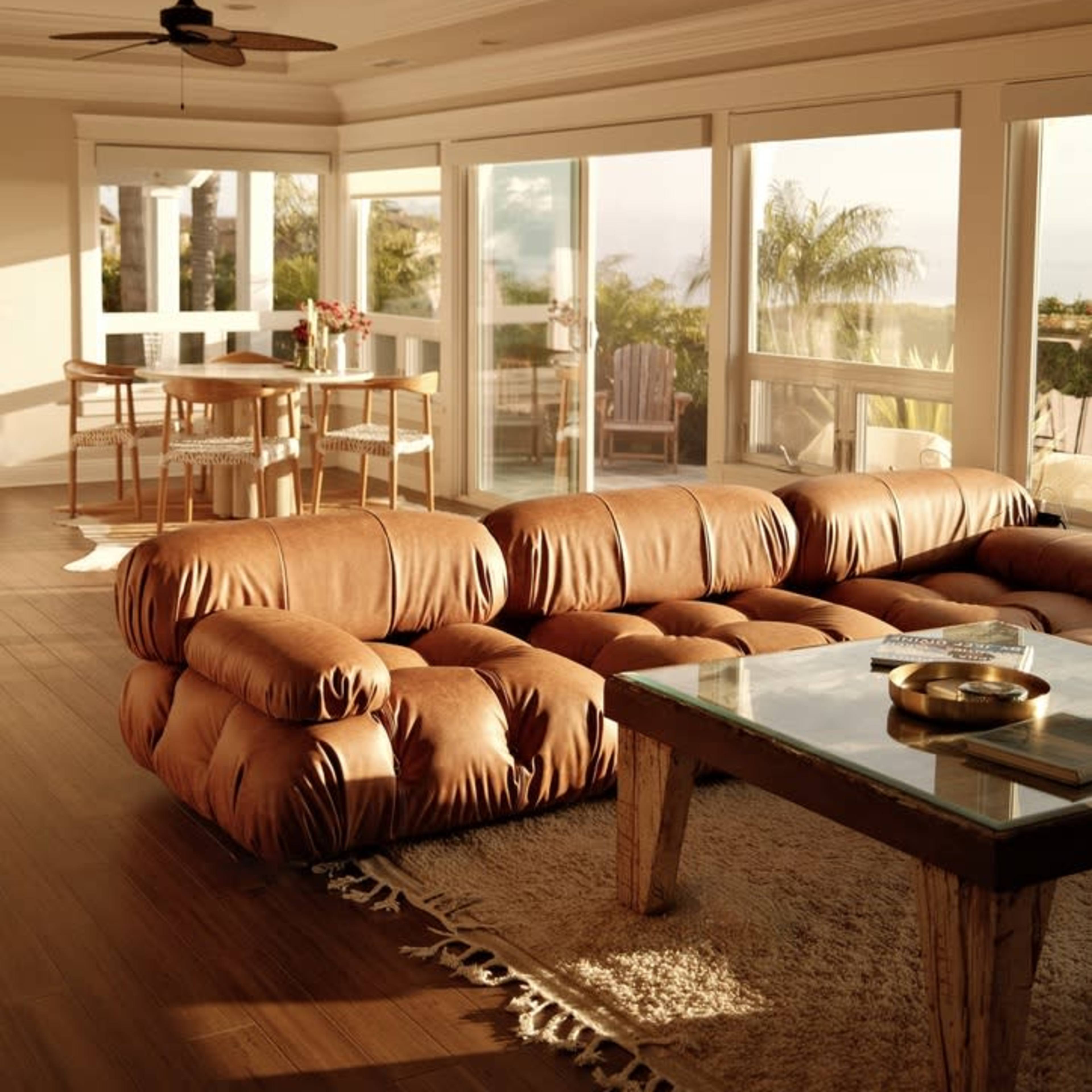 A spacious living room features a large brown sectional sofa, a wooden coffee table, and a dining area with tall chairs, illuminated by natural light from large windows.