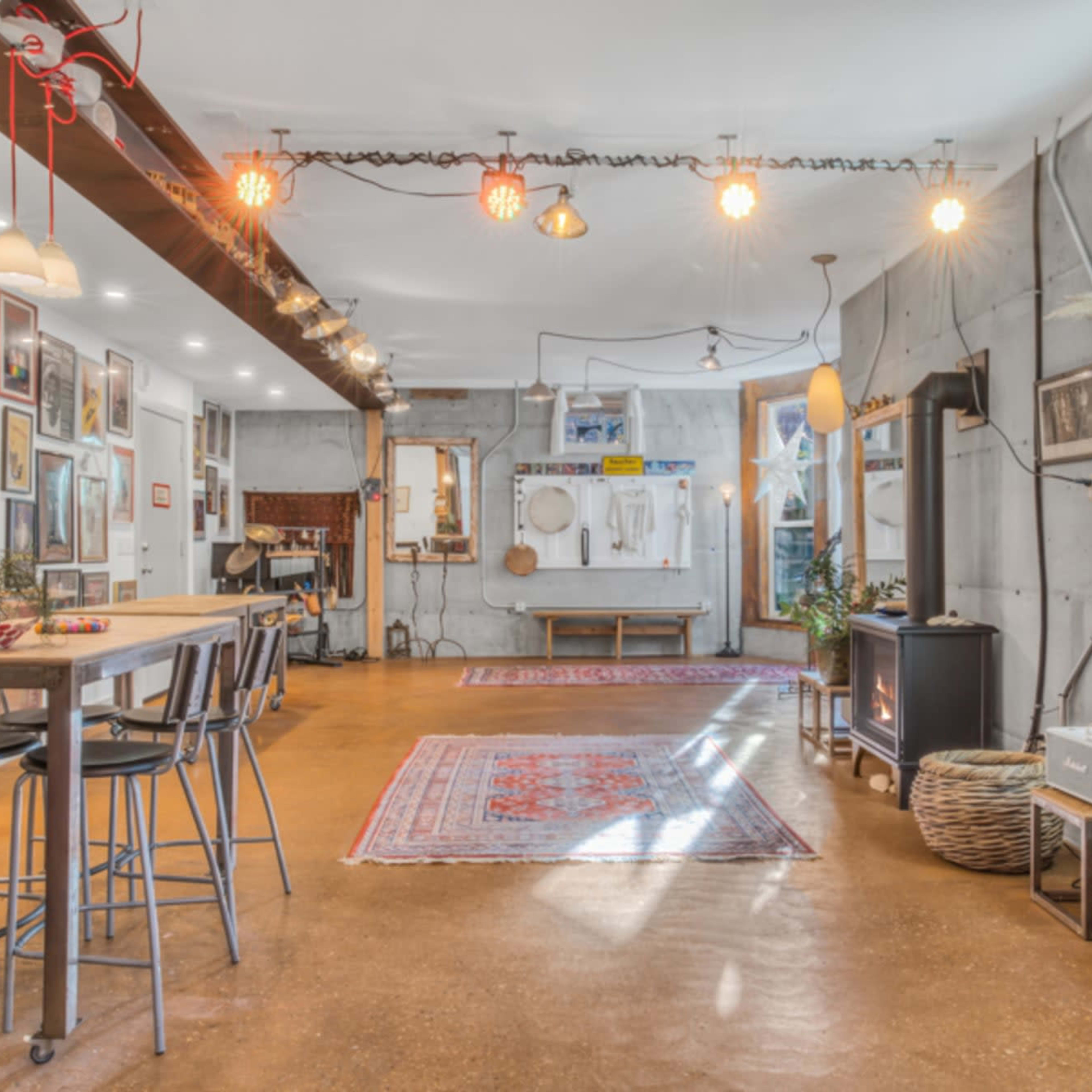 A spacious interior with concrete walls, a mixed lighting setup, and various decorations including rugs and artwork on the walls.