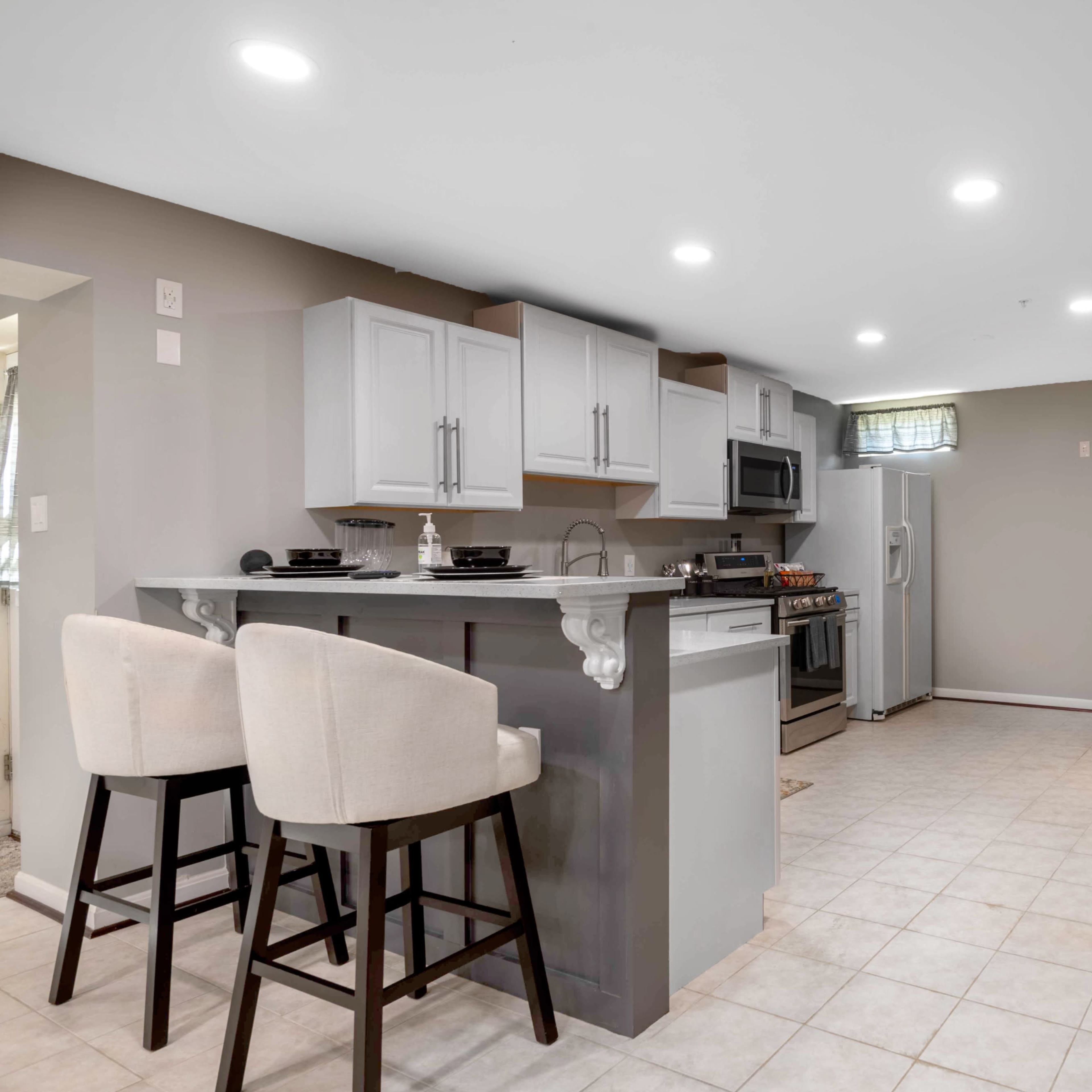 A modern kitchen and bar area with gray cabinetry, stainless steel appliances, and a seating area at a counter.