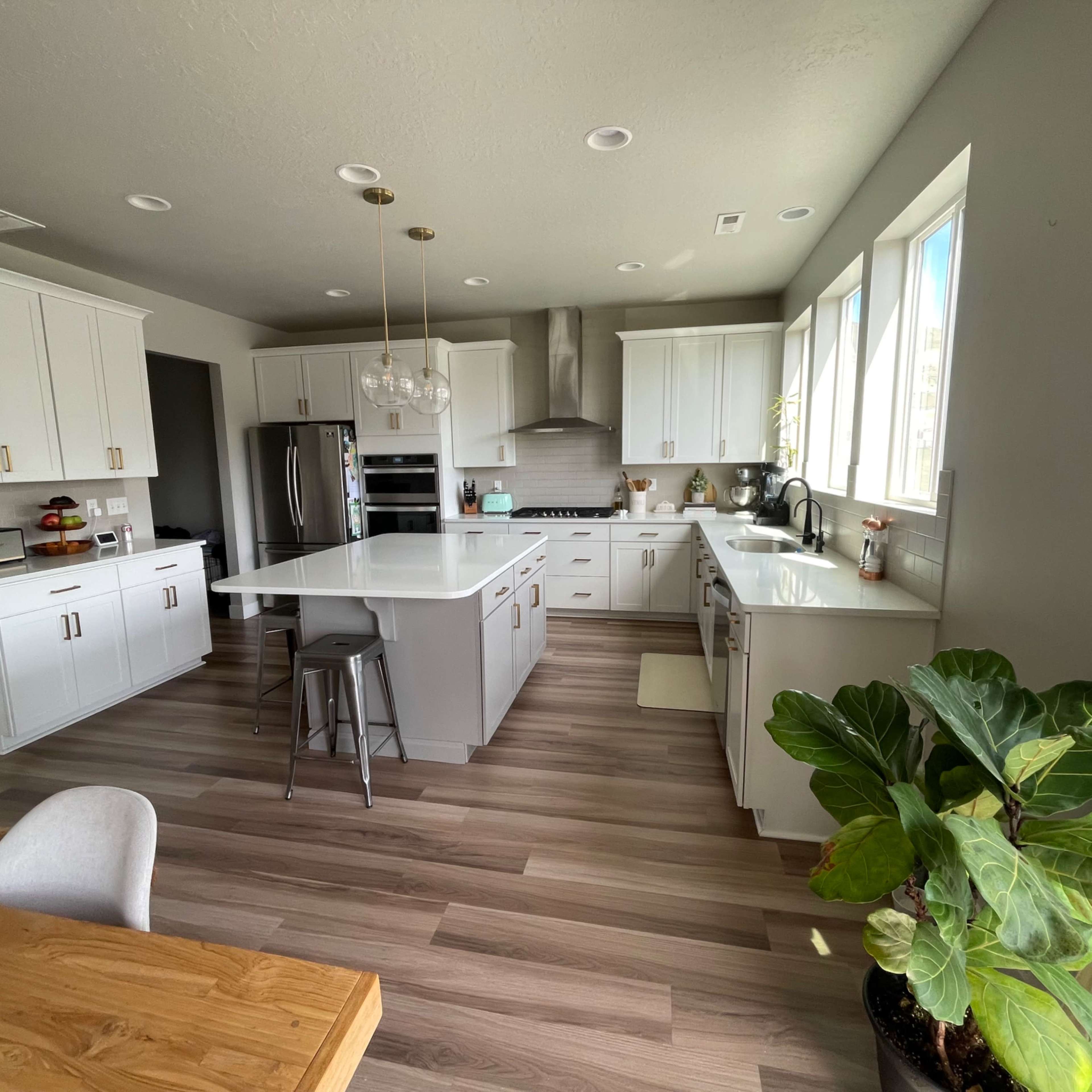 The kitchen features white cabinetry, an island with seating, stainless steel appliances, and large windows allowing natural light.