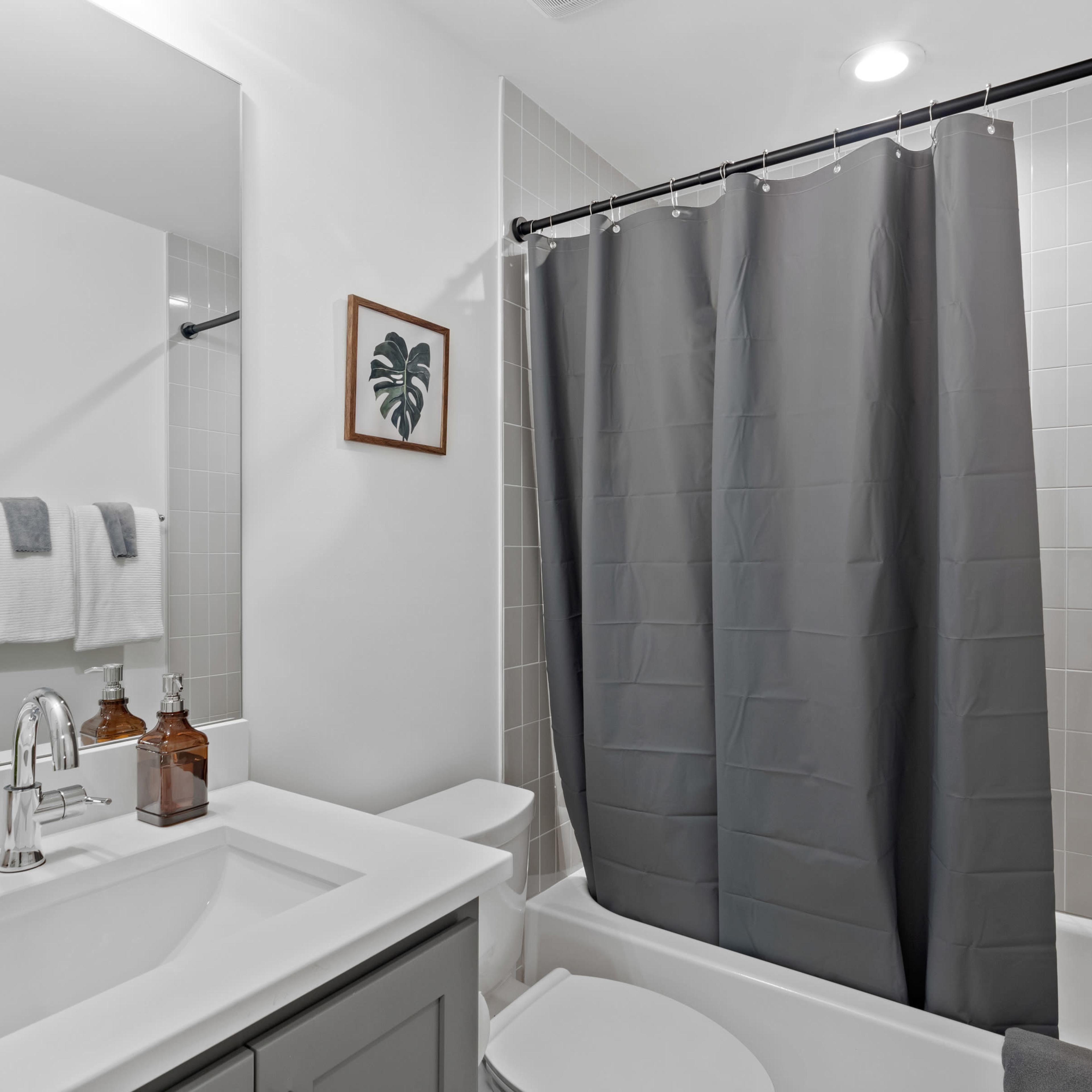 A modern bathroom featuring a gray shower curtain, a white sink with a mirror, and neatly arranged towels and decorative plants.