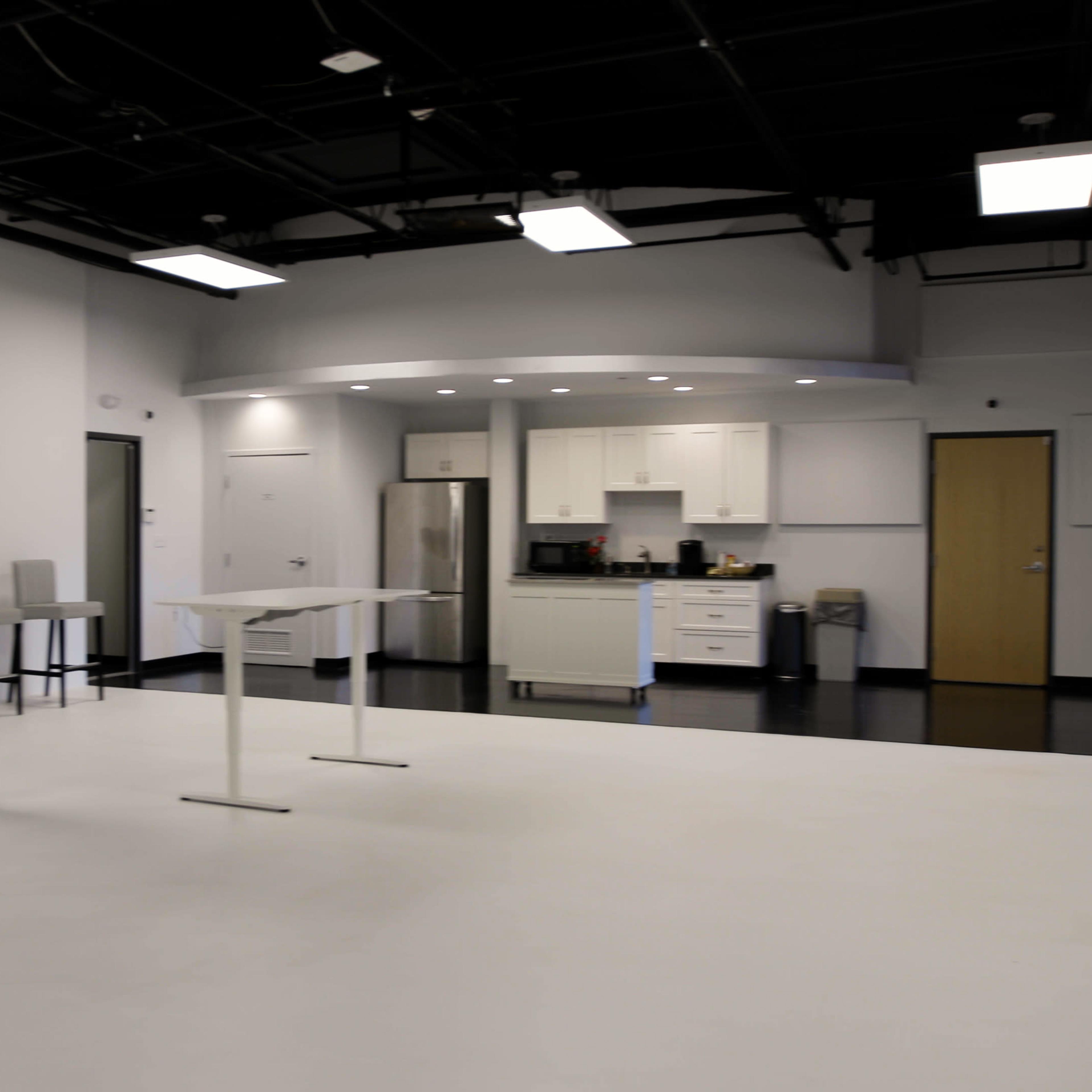 A spacious, modern kitchen area with white walls, a central table, and several barstools.