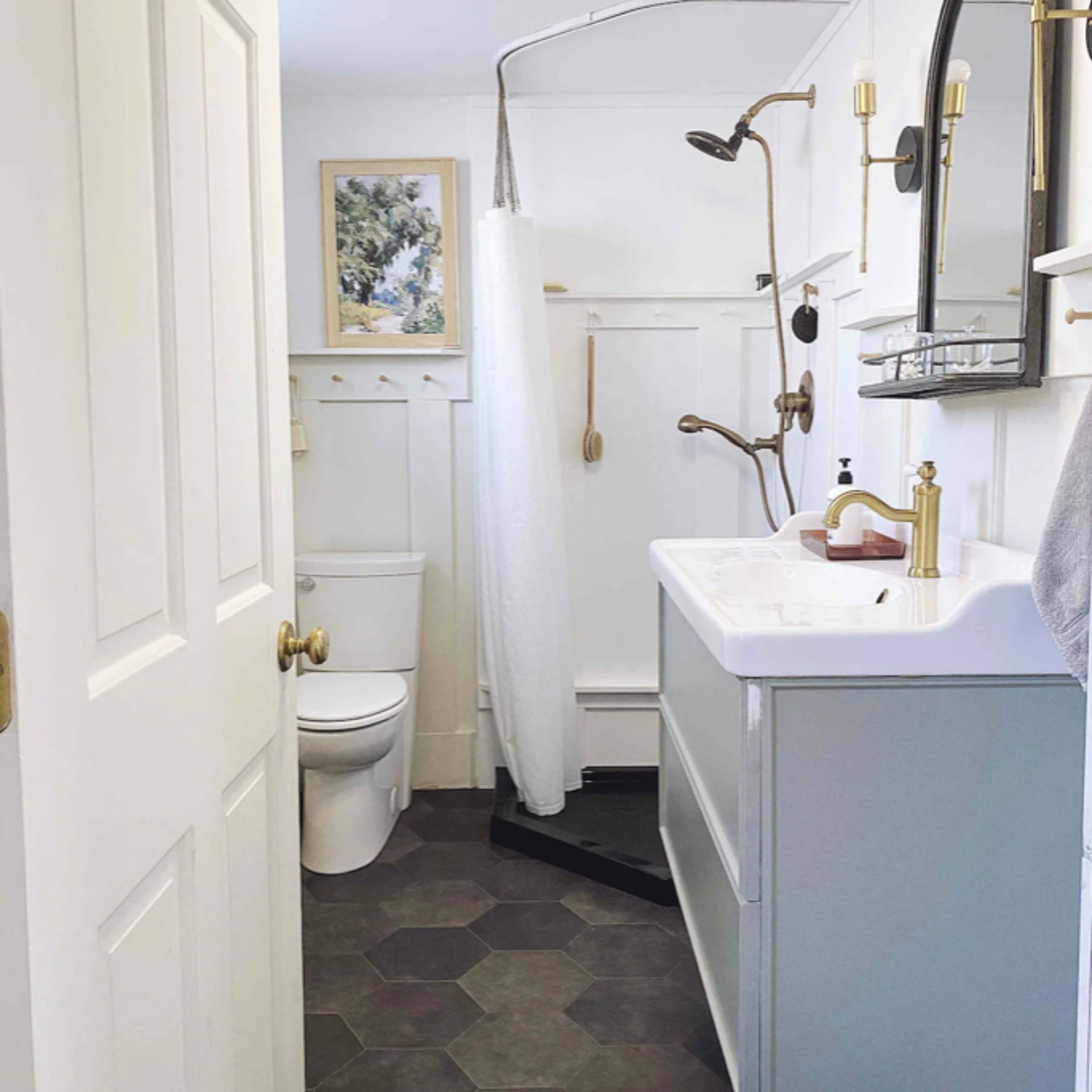 A compact bathroom features a shower area, a white sink with a gold faucet, a toilet, and a mirror above the sink, with hexagon-shaped floor tiles.