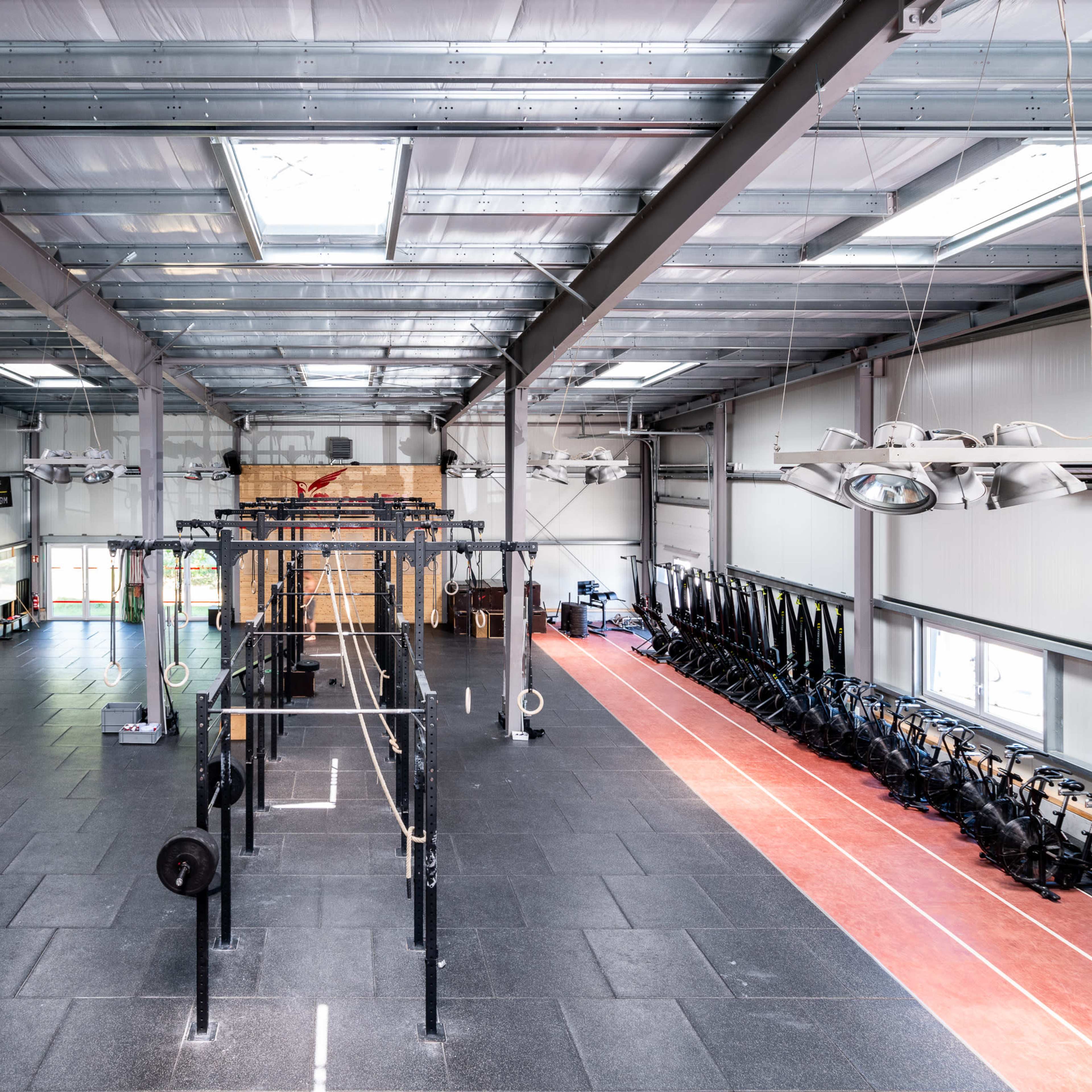 A spacious indoor gym with a central area for weightlifting and rows of rowing machines along one side.