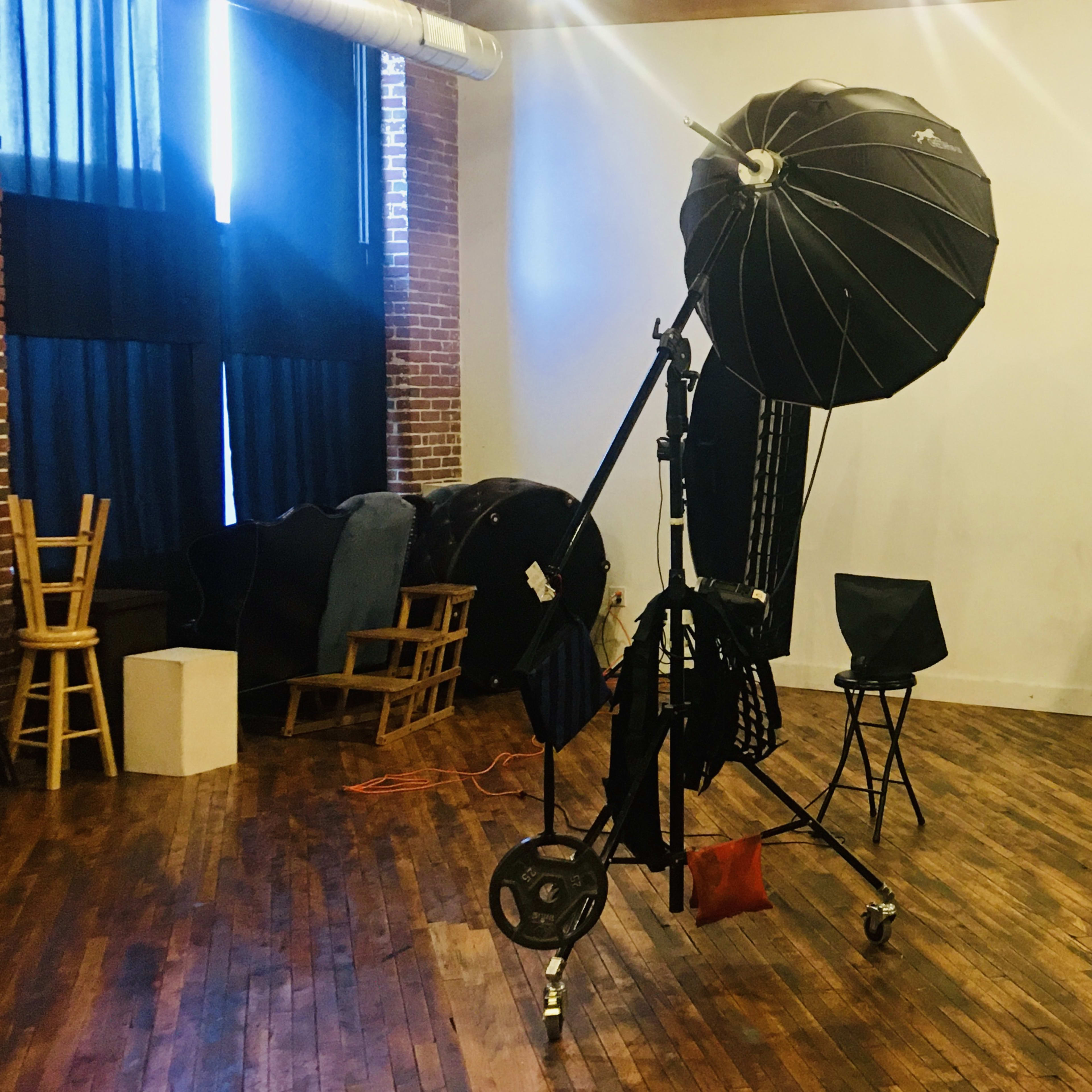 A photography studio features various lighting equipment, including softboxes and a backdrop, set up on a wooden floor.