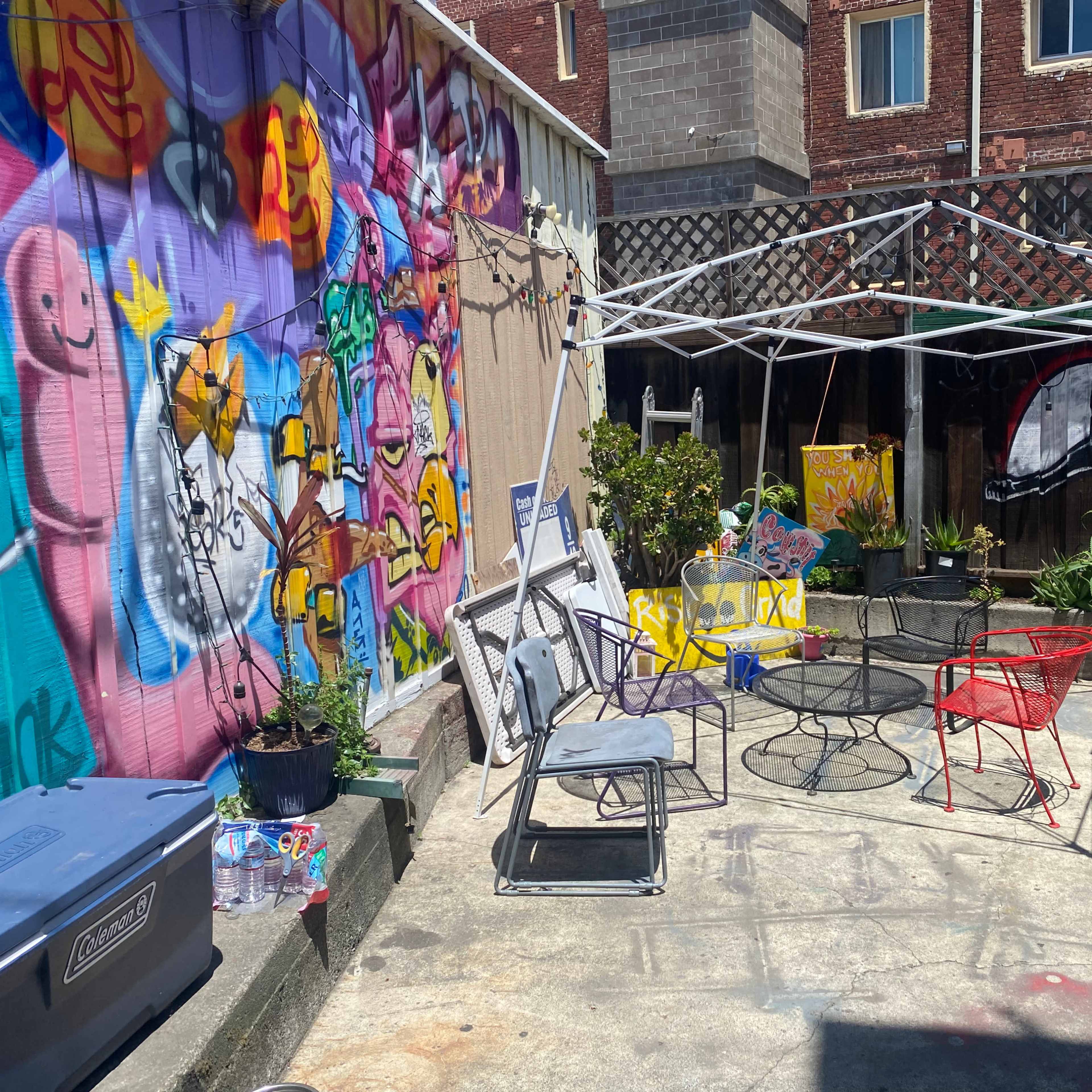 An outdoor space with a white canopy, several chairs, and colorful murals on the walls.