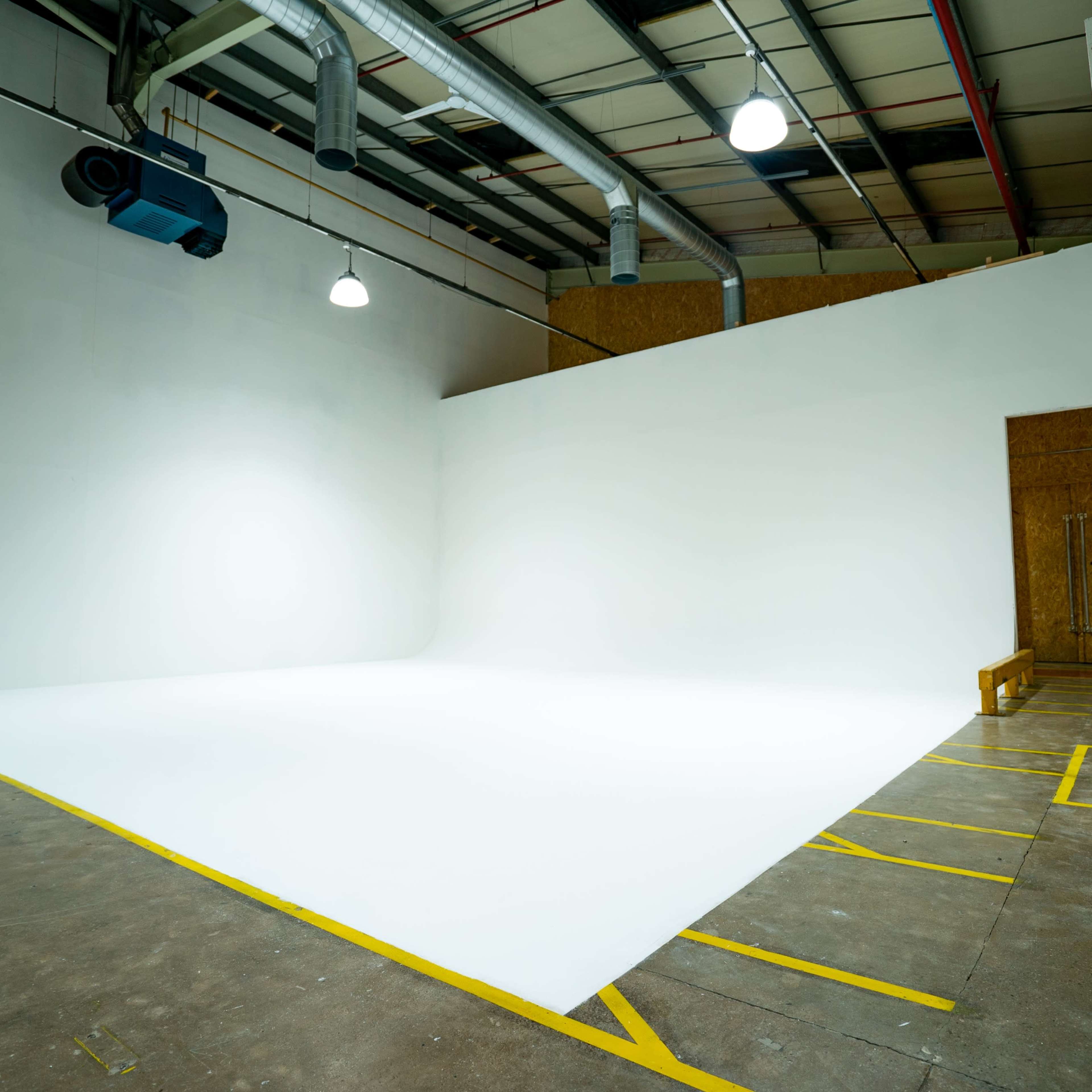 An empty photography studio features a seamless white backdrop, with overhead lights and exposed structural elements.