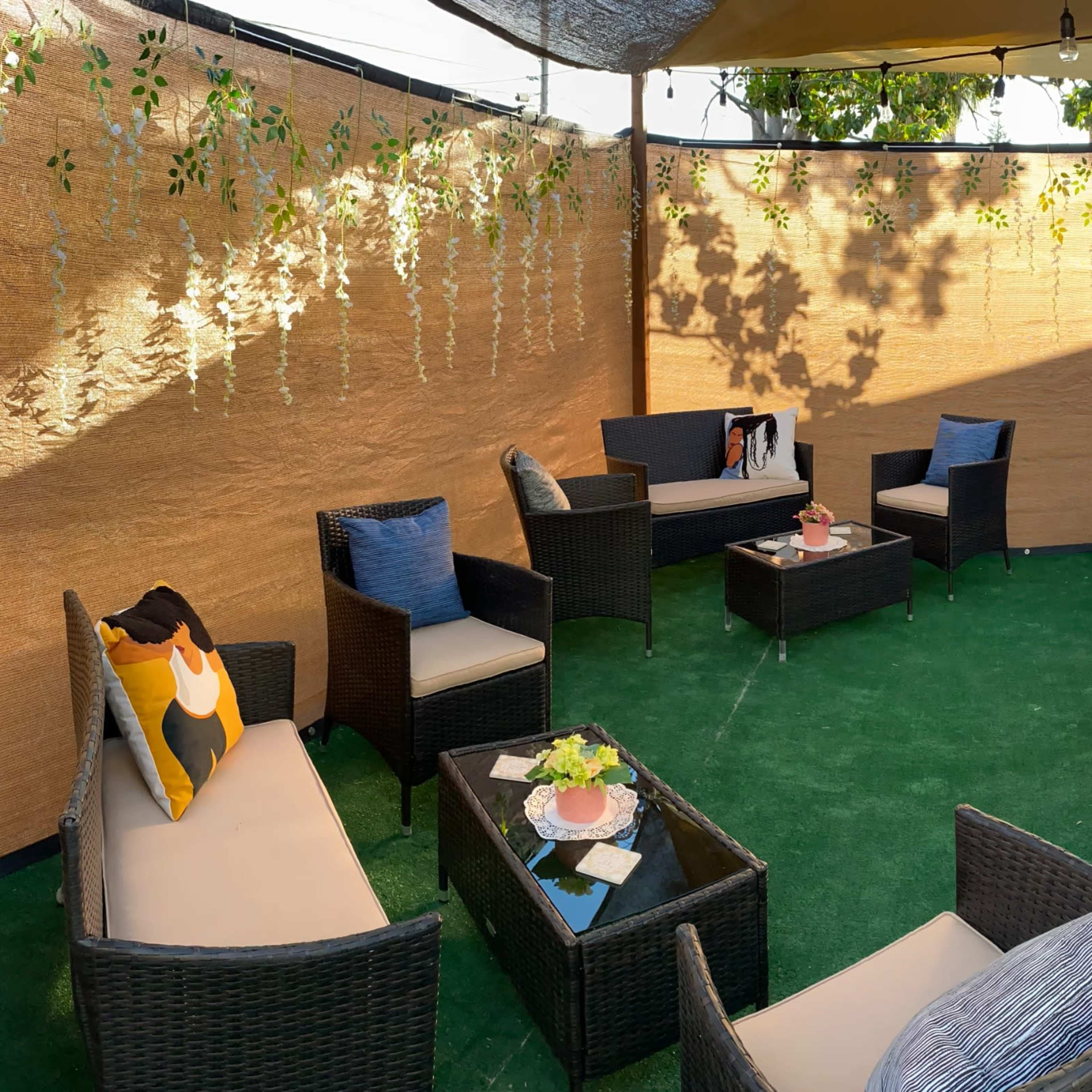 A decorated outdoor seating area with lounge chairs, a table set with gifts, and greenery hanging from overhead structures.