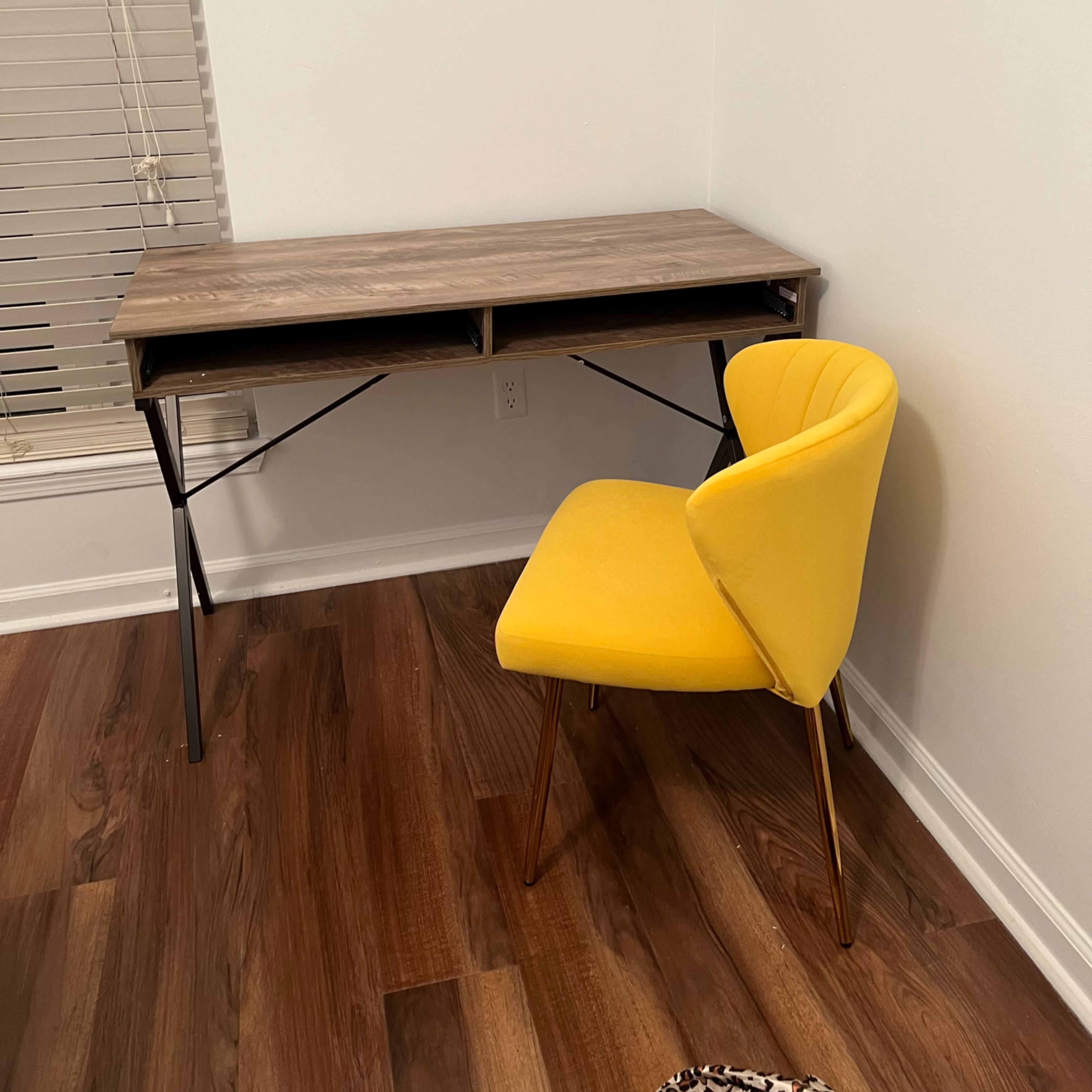 A wooden desk with a folding design is positioned against a wall beside a yellow chair with gold legs.