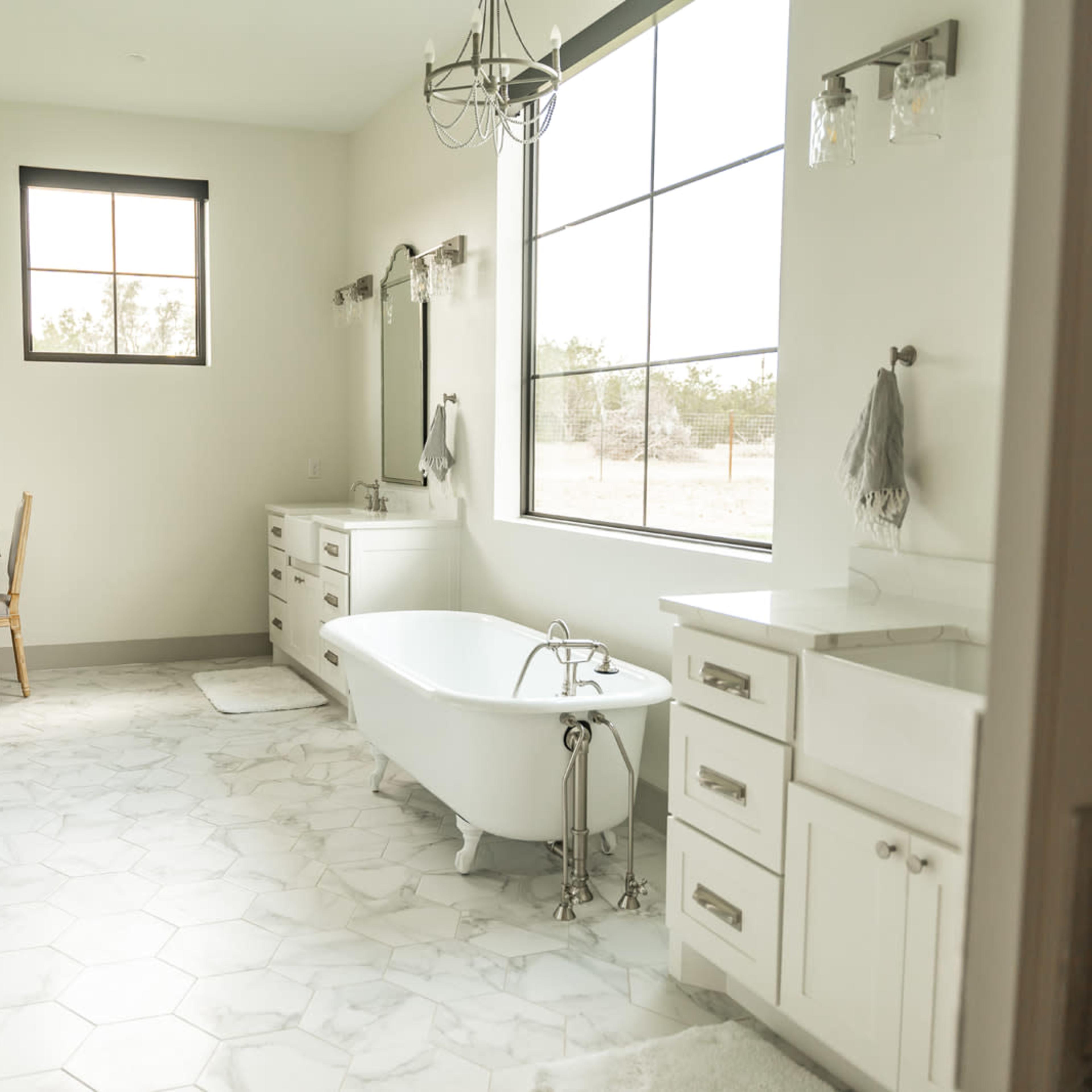 A spacious bathroom features a freestanding tub, double vanities, a large window, and a shower area.