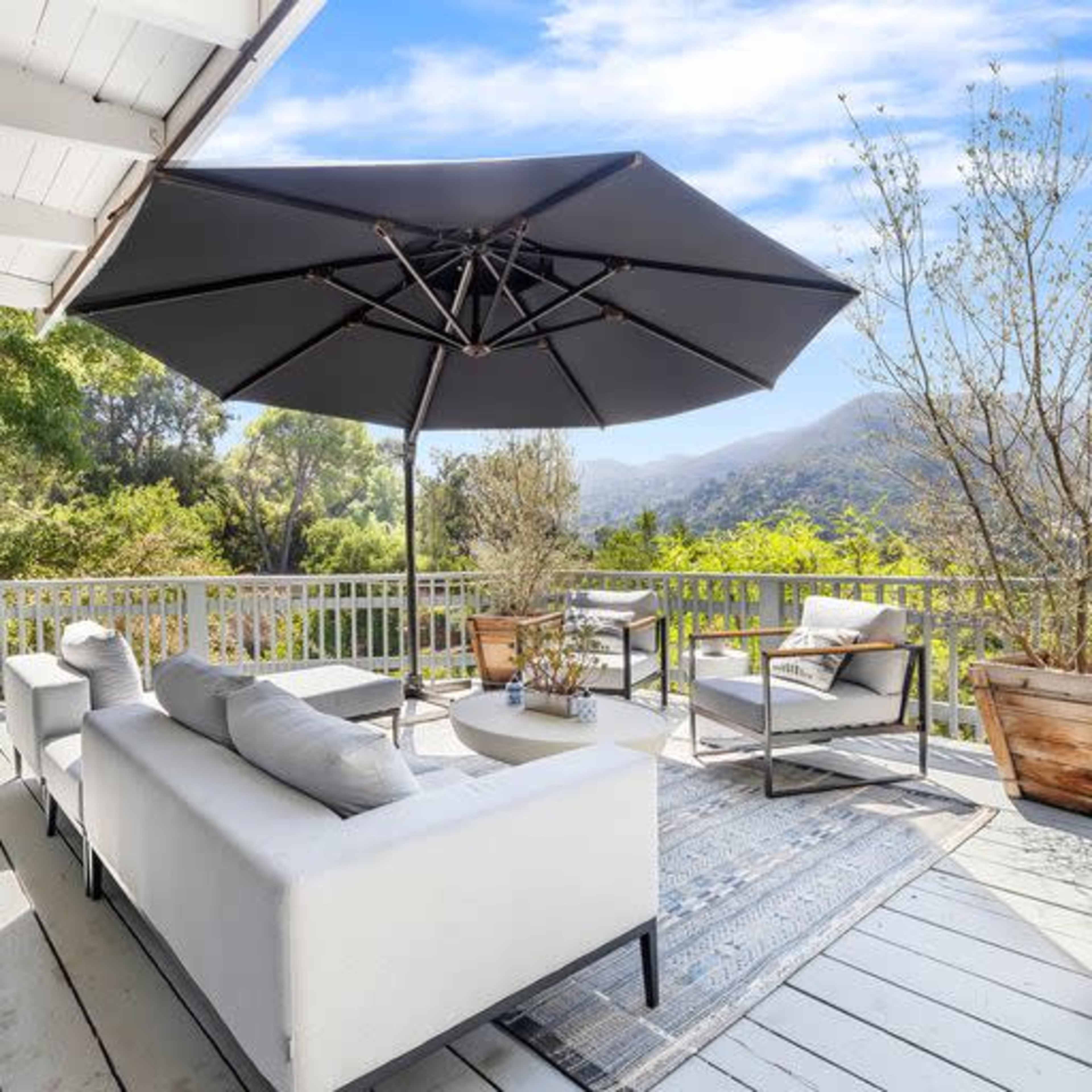 A shaded outdoor seating area features a sofa and chairs, with a view of trees and mountains in the background.