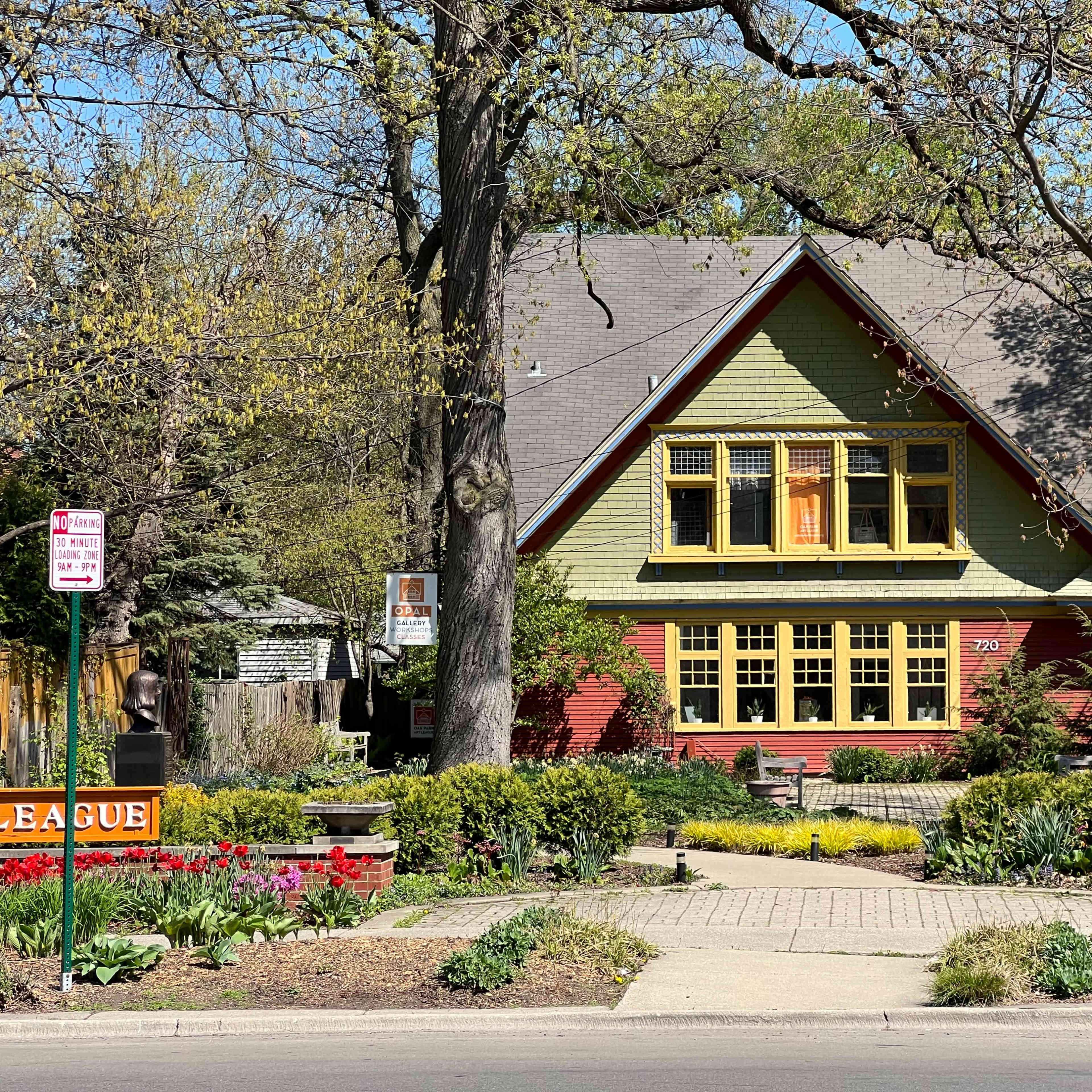 A large green and red house with yellow trim is surrounded by a well-kept garden full of flowers and trees.