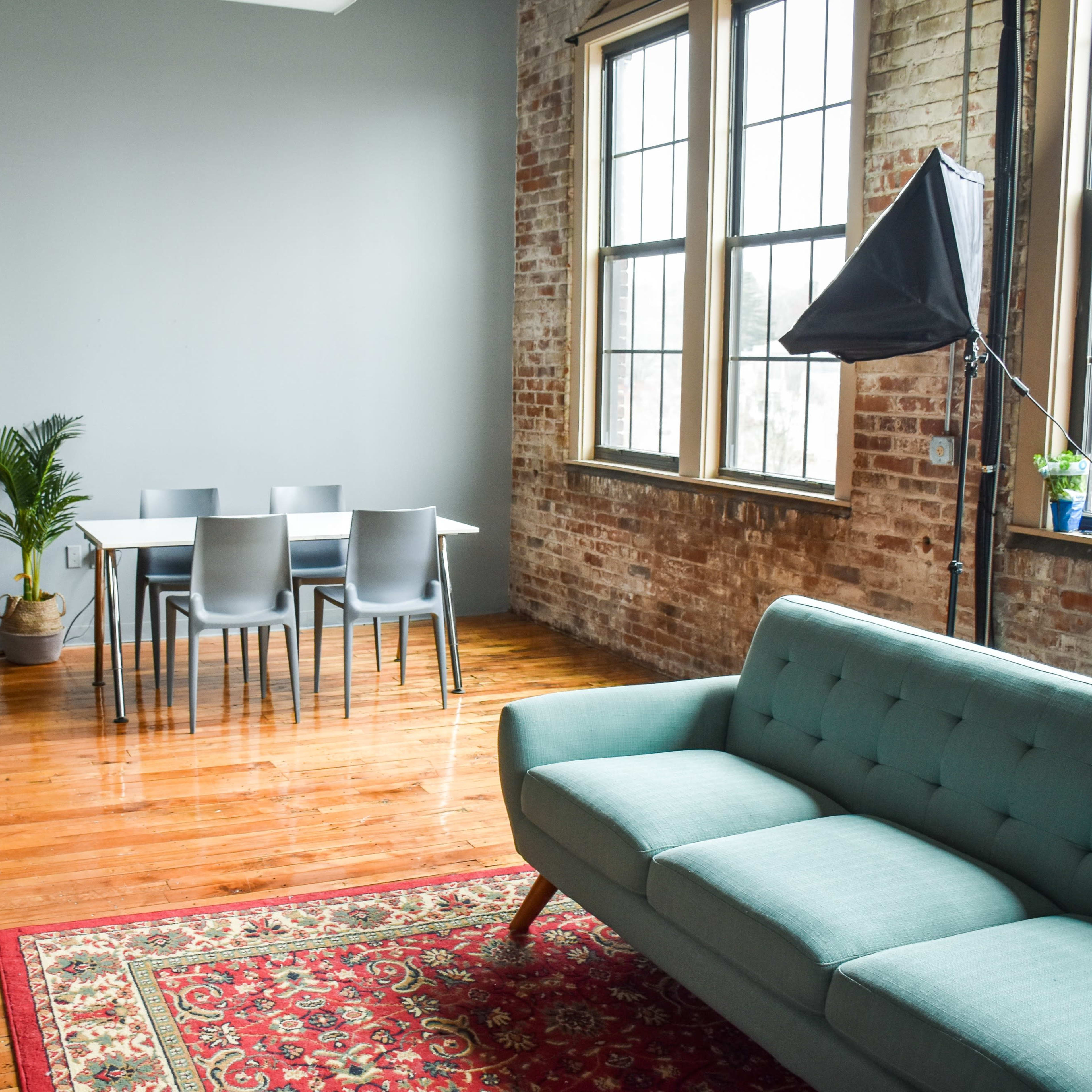 A bright room with a table and chairs in the center, flanked by studio lights, a plant, and a couch on a patterned rug.