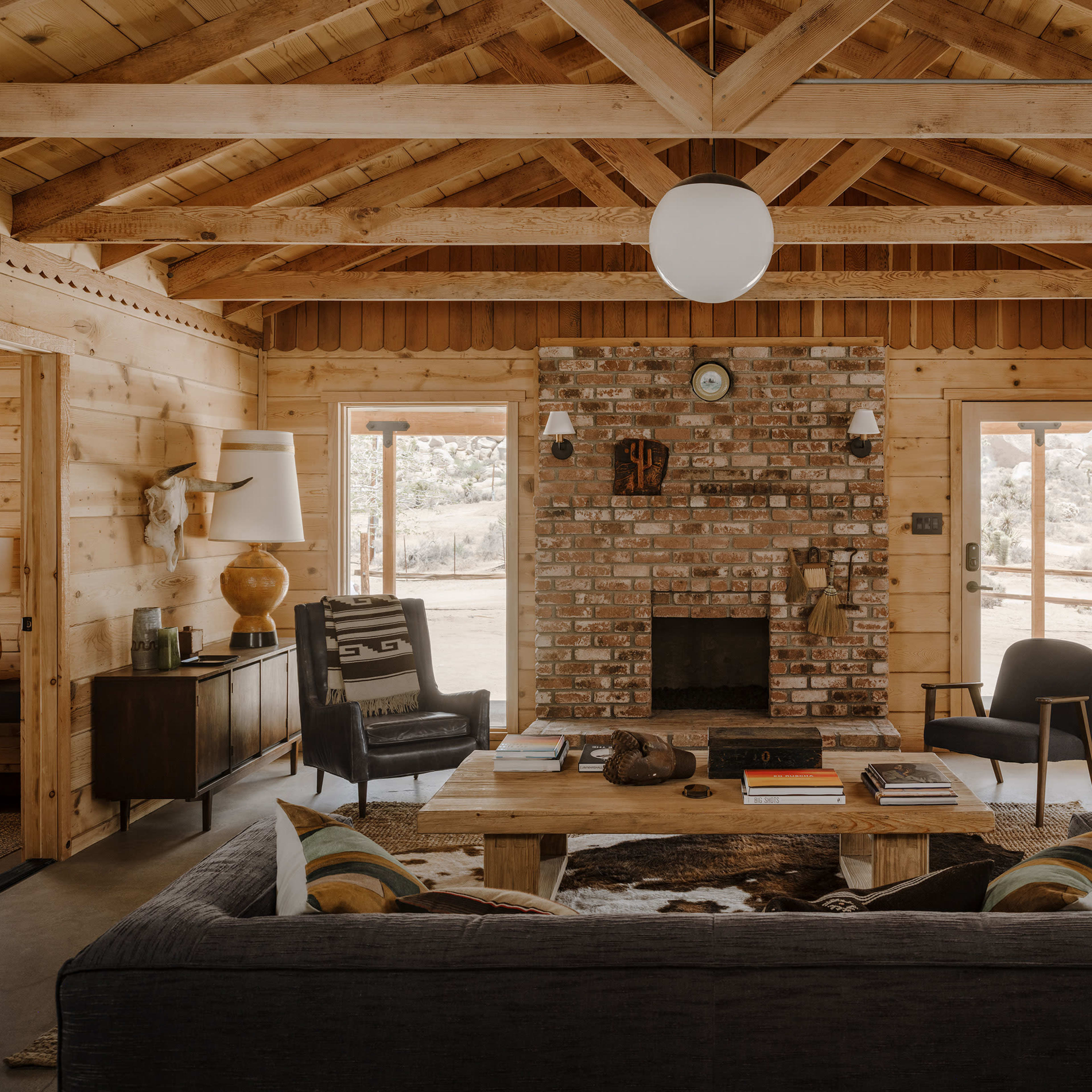 A cozy interior of a wooden cabin with a brick fireplace, a large sofa, and rustic furniture.