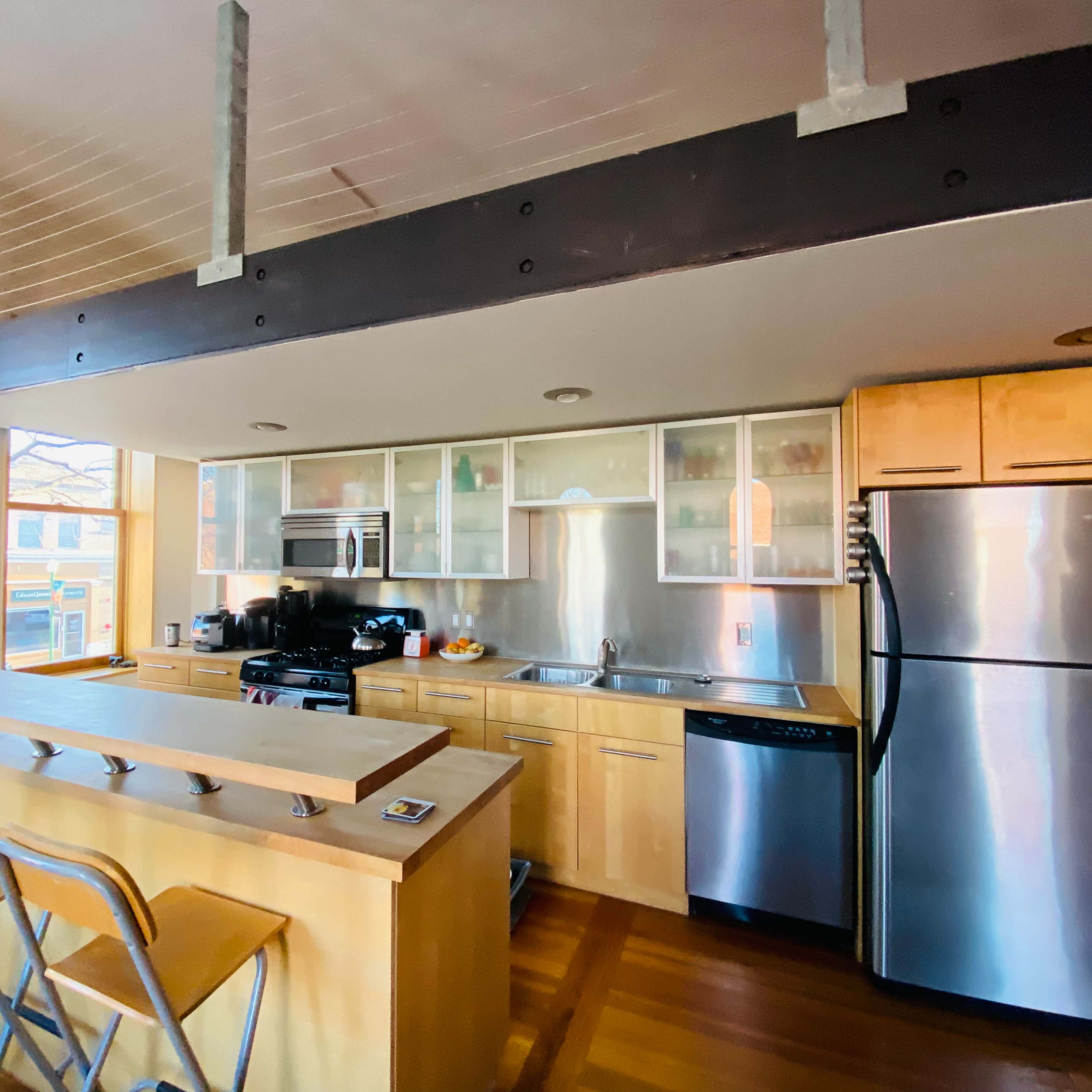 A modern kitchen with wooden cabinetry, stainless steel appliances, and a raised countertop with barstools.