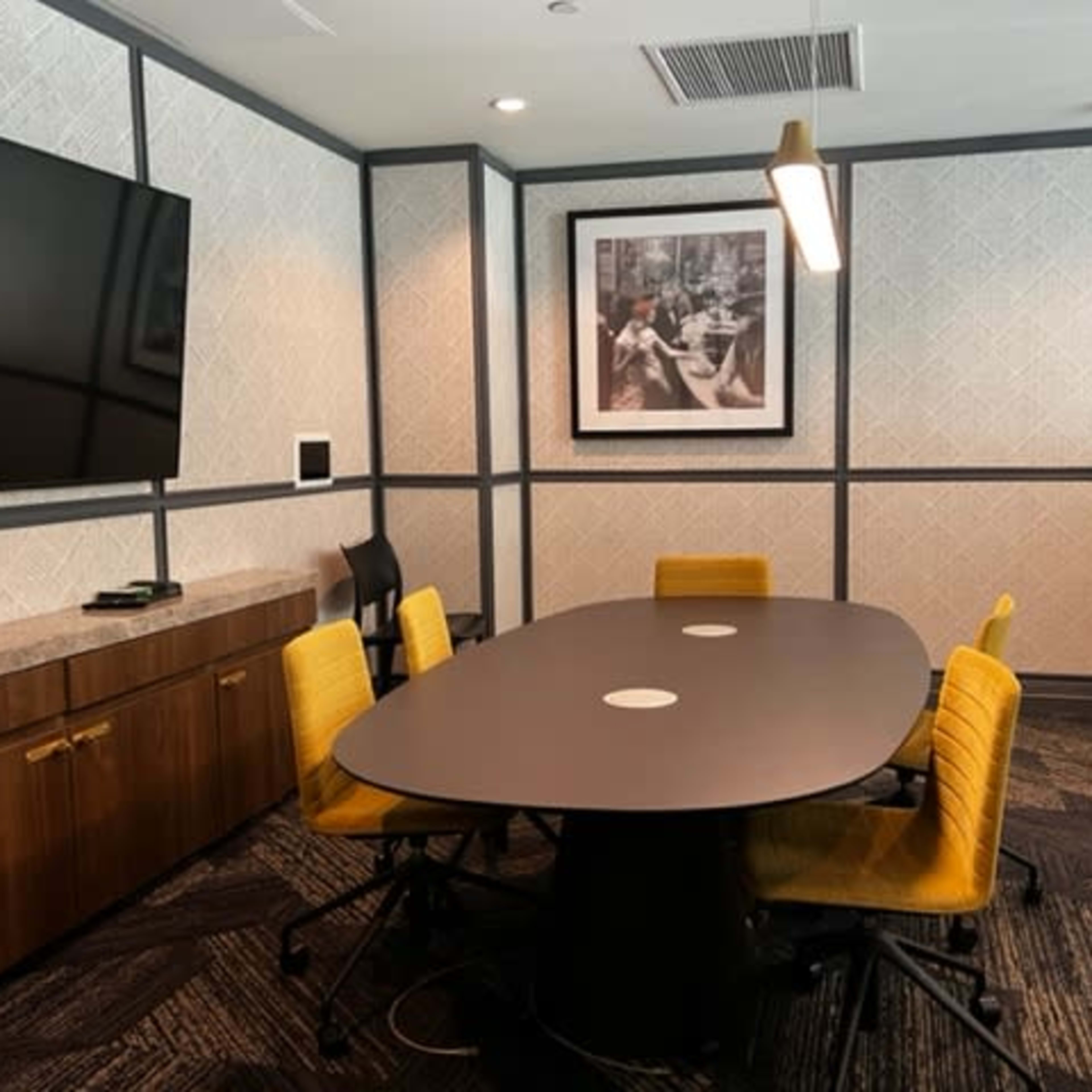 A modern conference room with a circular table surrounded by yellow chairs, a mounted television, and framed artwork on the wall.