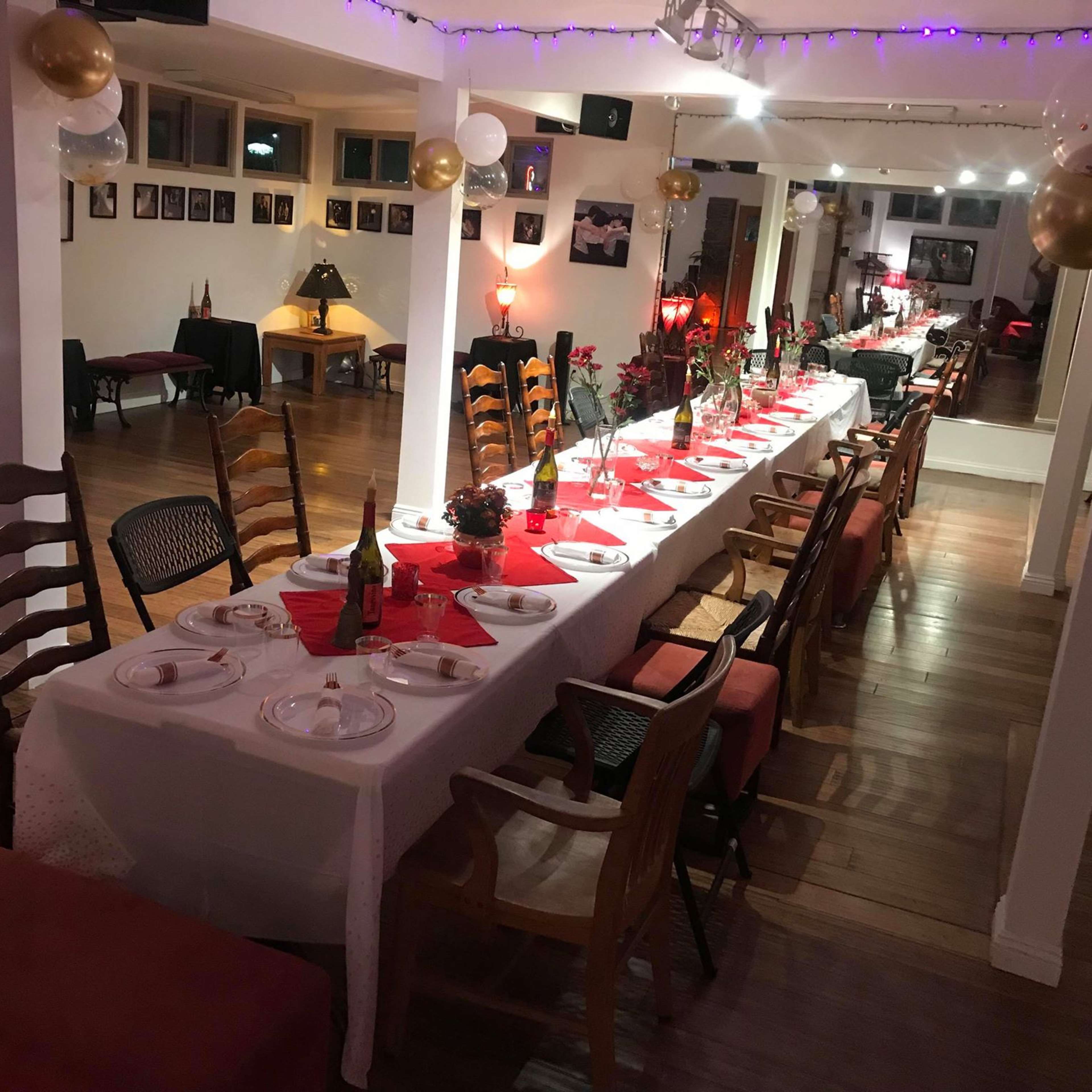 A long dining table is set with plates and glasses in a warmly lit room decorated with balloons and photographs on the walls.