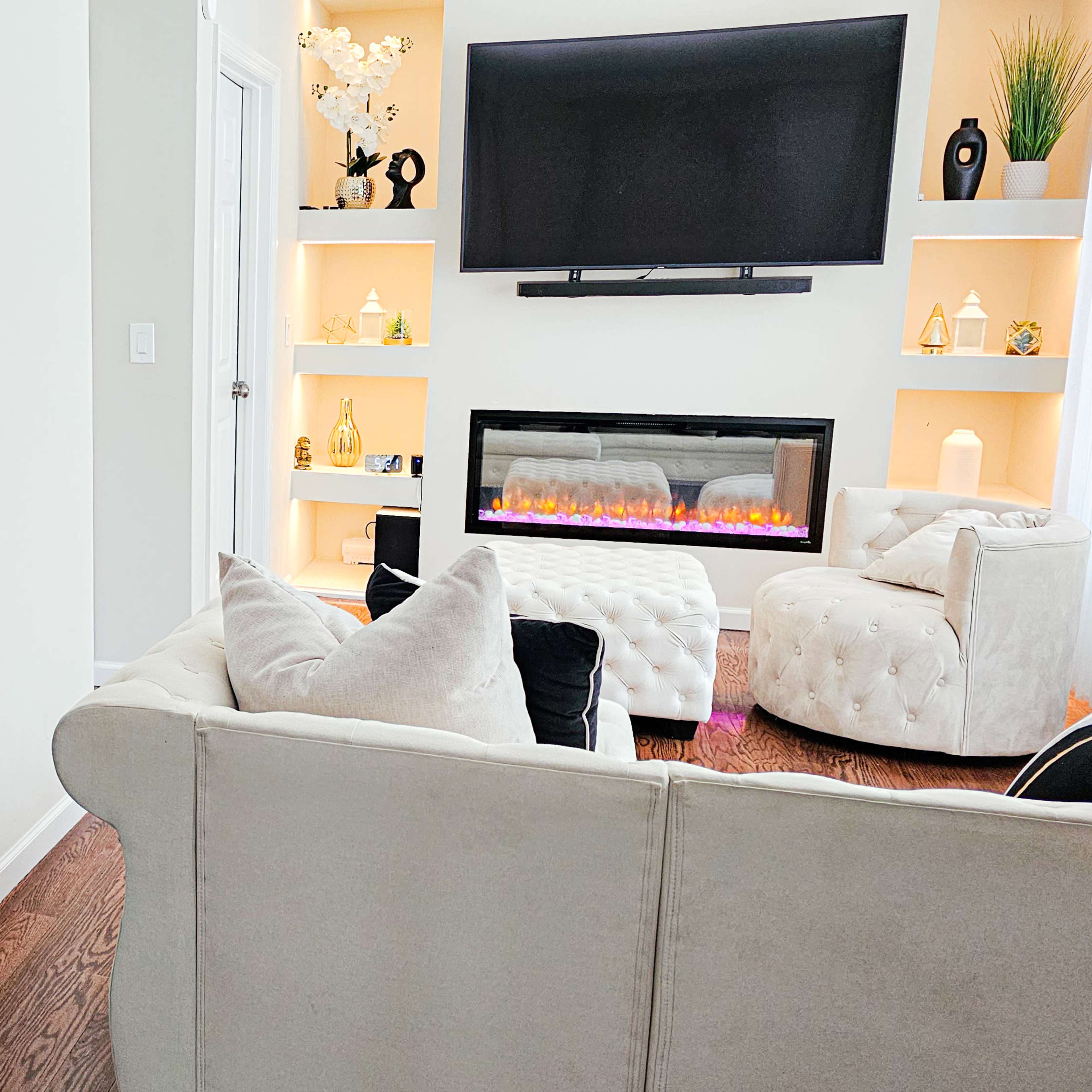 A modern living room with a piano on the left, a cozy couch, and an electric fireplace beneath a wall-mounted television.