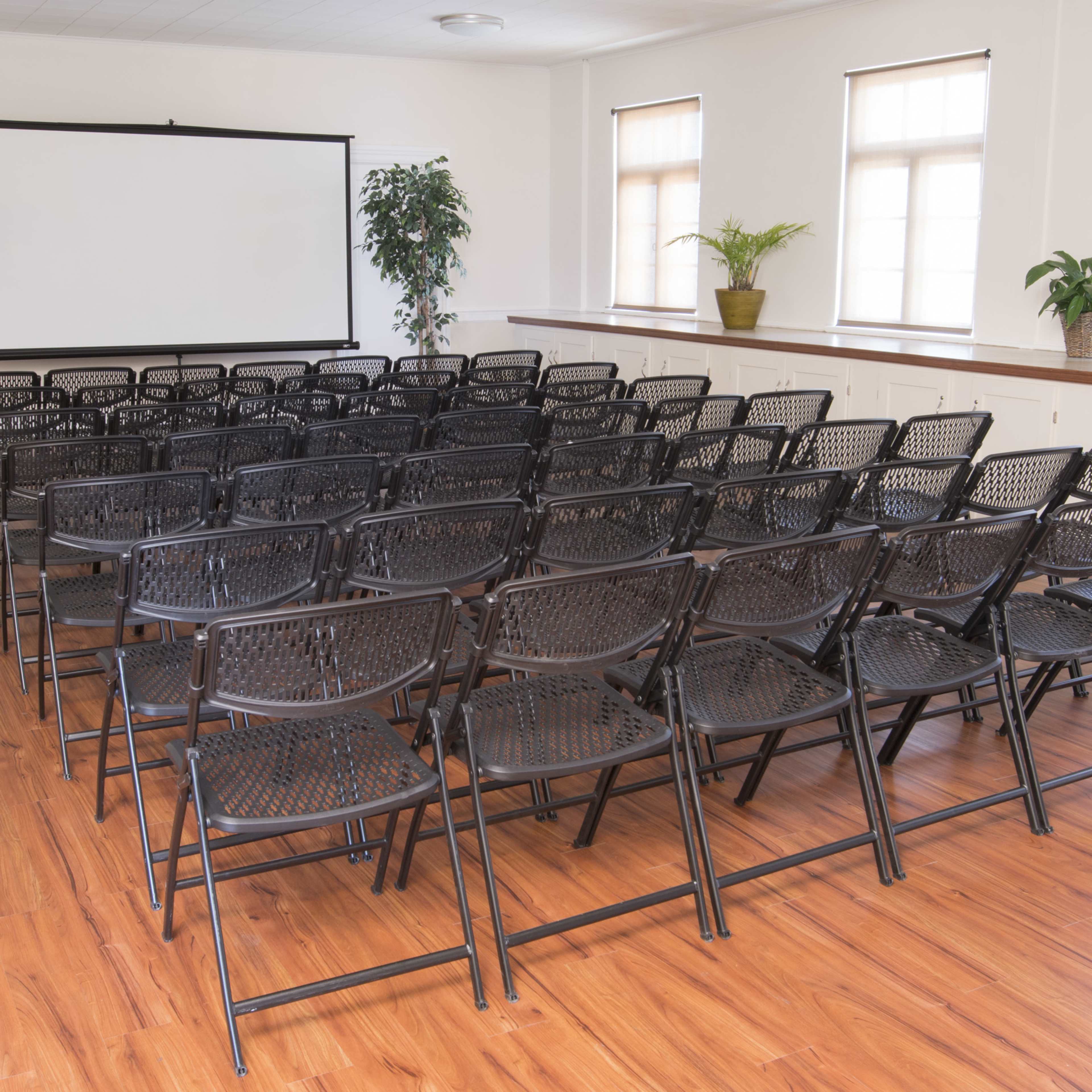 A room set up with rows of black folding chairs facing a blank projection screen.