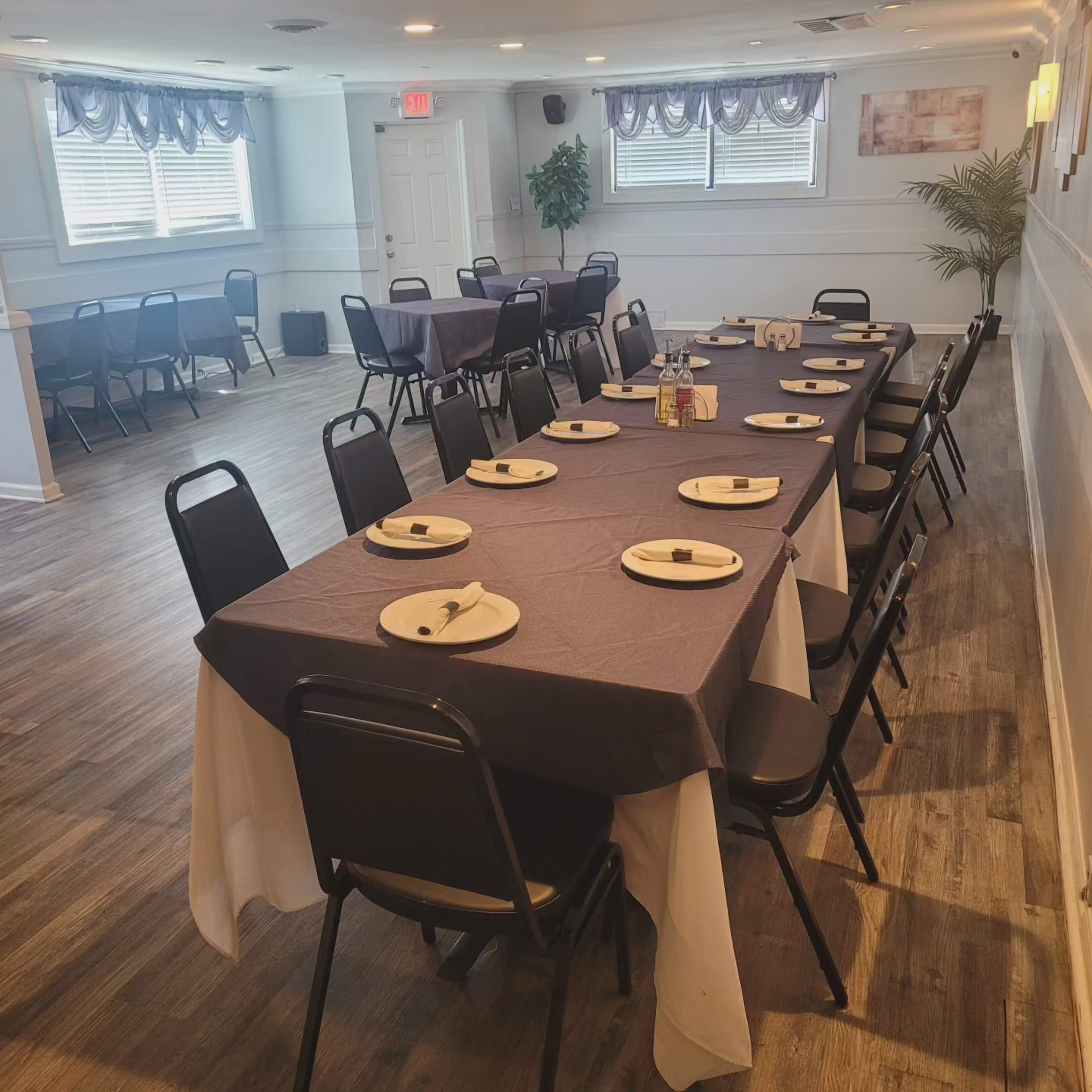 A dining room is set with tables covered in purple and white tablecloths, arranged with plates and utensils, ready for a gathering.