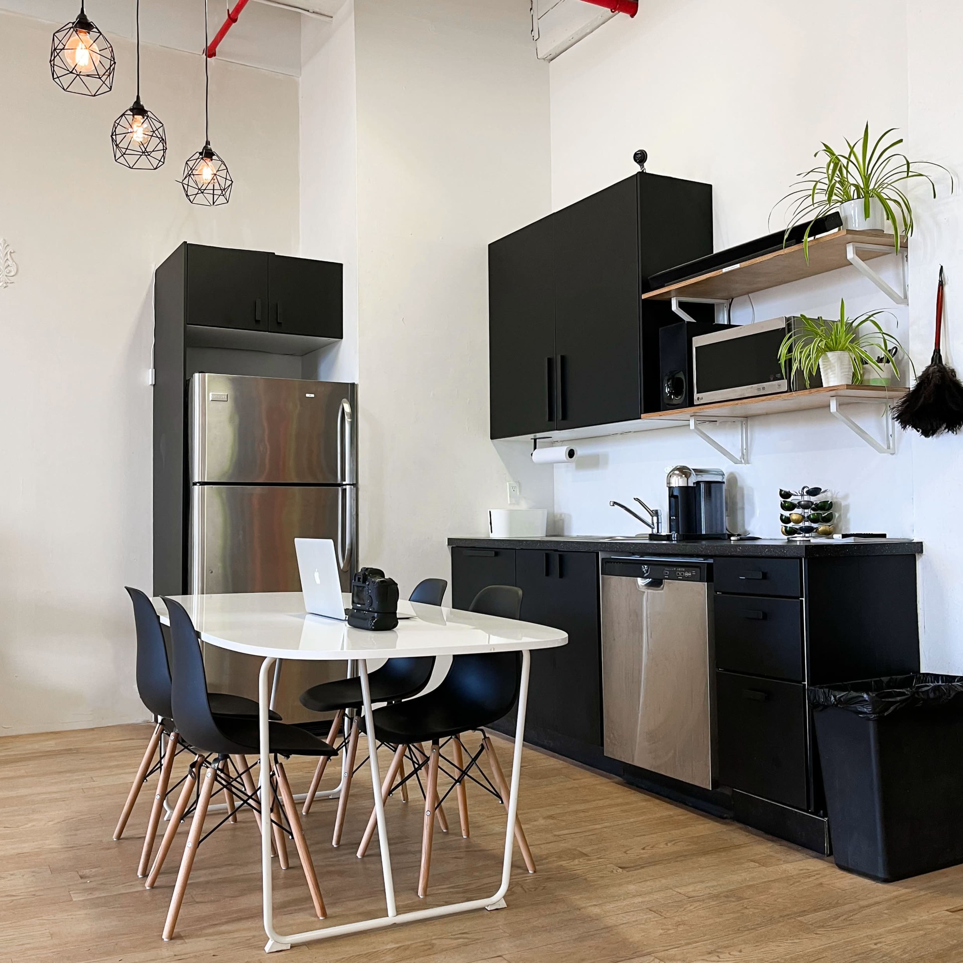 A modern kitchen with black cabinetry, stainless steel appliances, a white table with black chairs, and pendant lighting.
