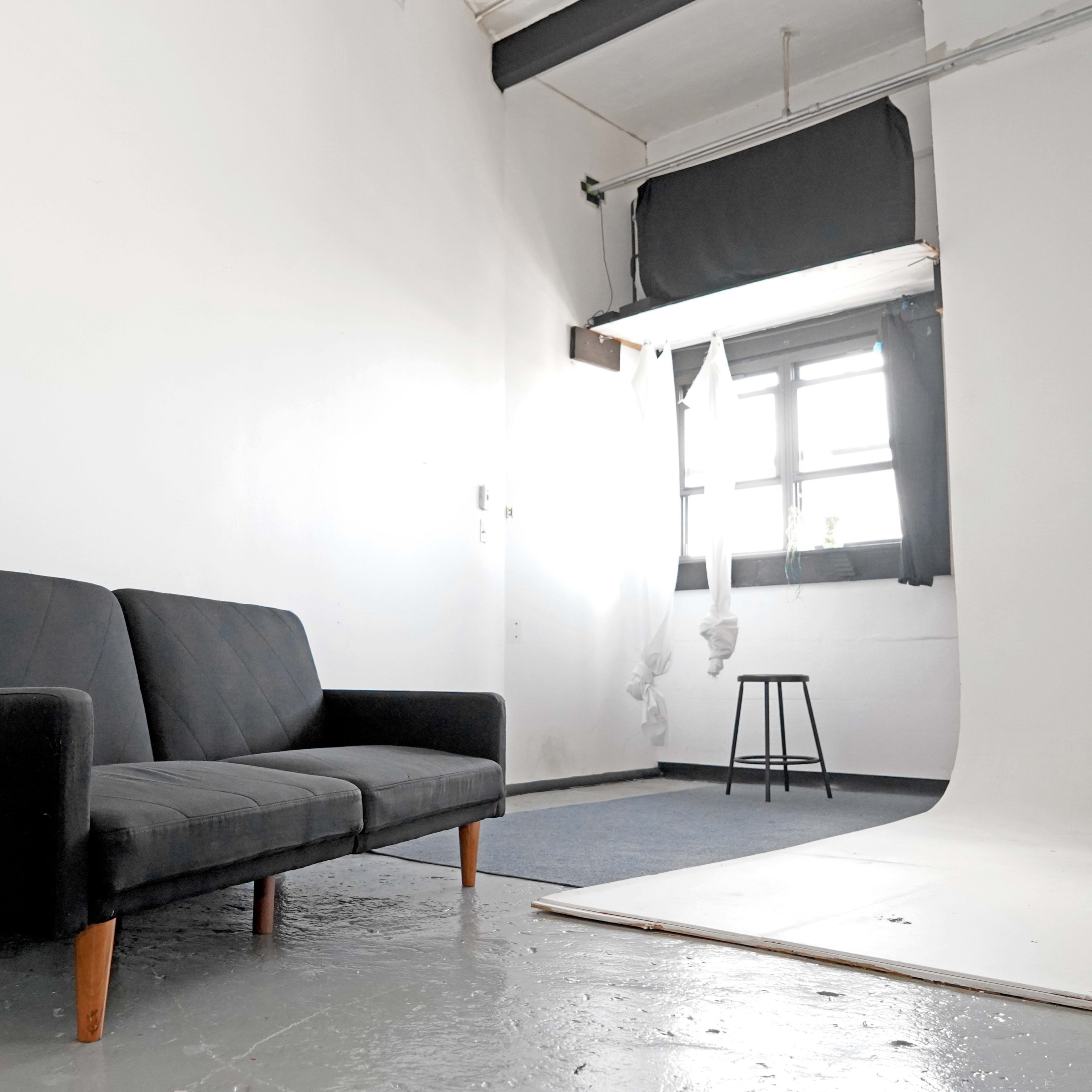 A minimalist studio space with a black couch, a stool, and a backdrop for photography.