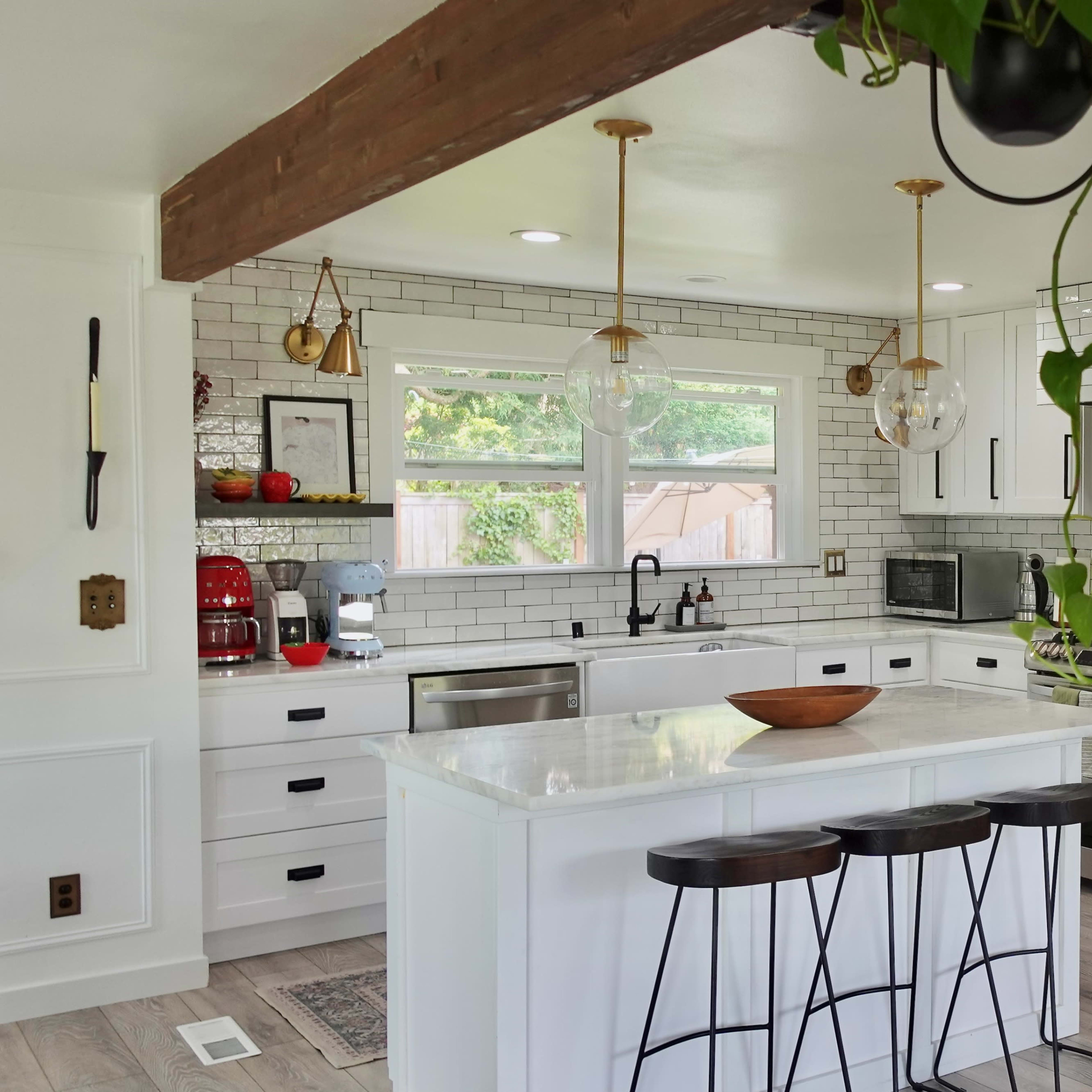 A modern kitchen features white cabinetry, a central island with bar stools, and a mix of stainless steel and black appliances.
