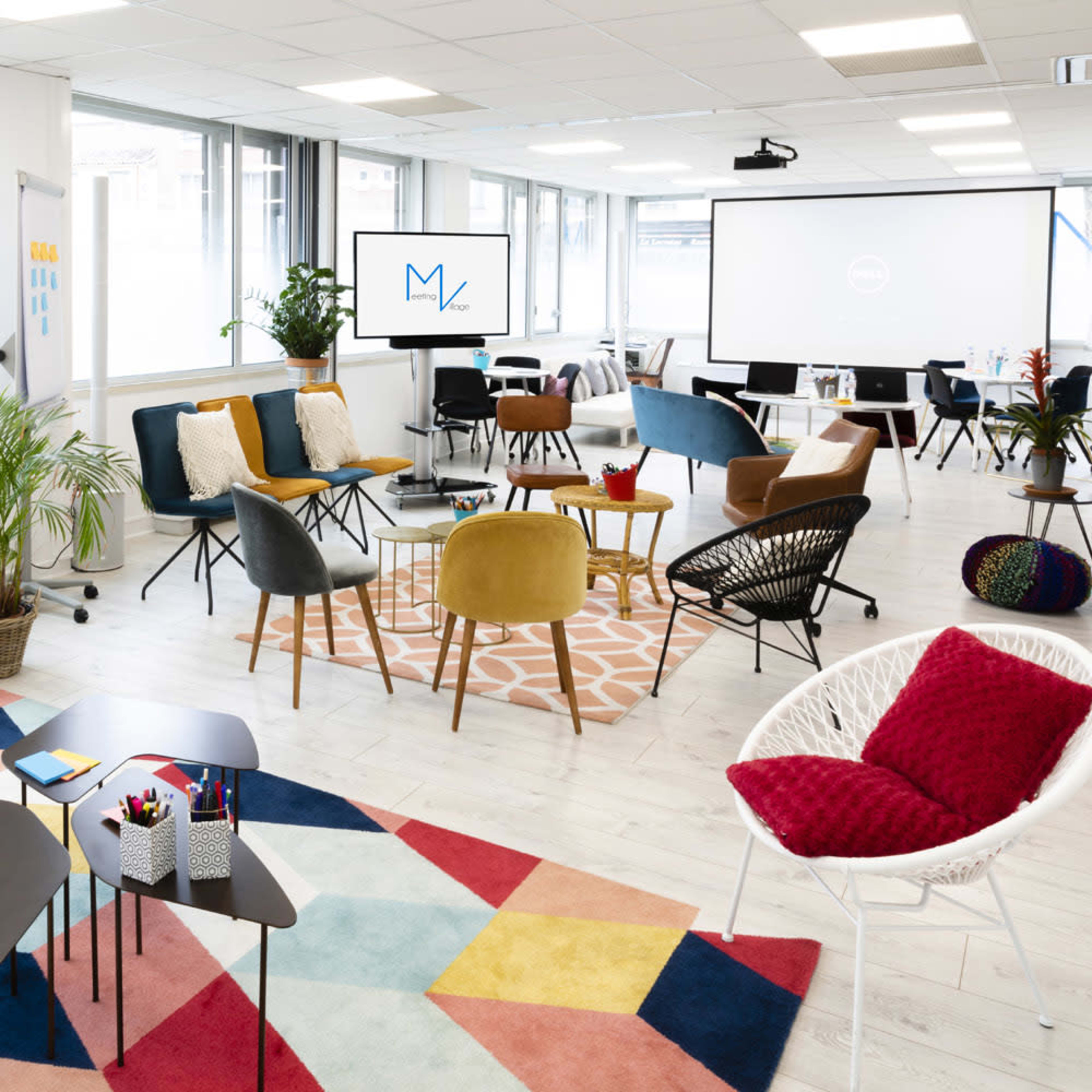 A modern office space with a variety of seating arrangements, colorful rugs, and presentation equipment.