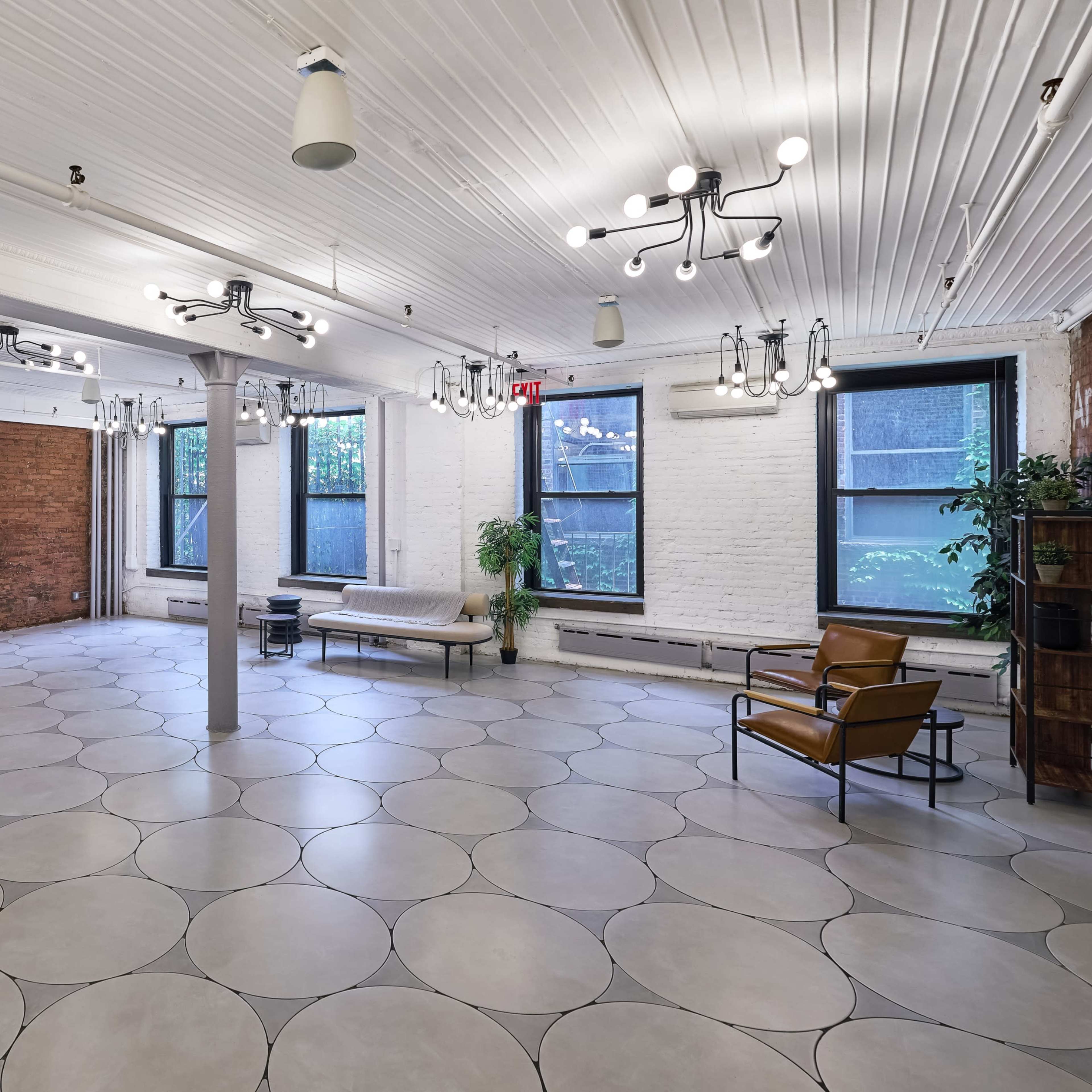A spacious, well-lit interior room with a patterned floor, large windows, and a mix of modern and industrial design elements.
