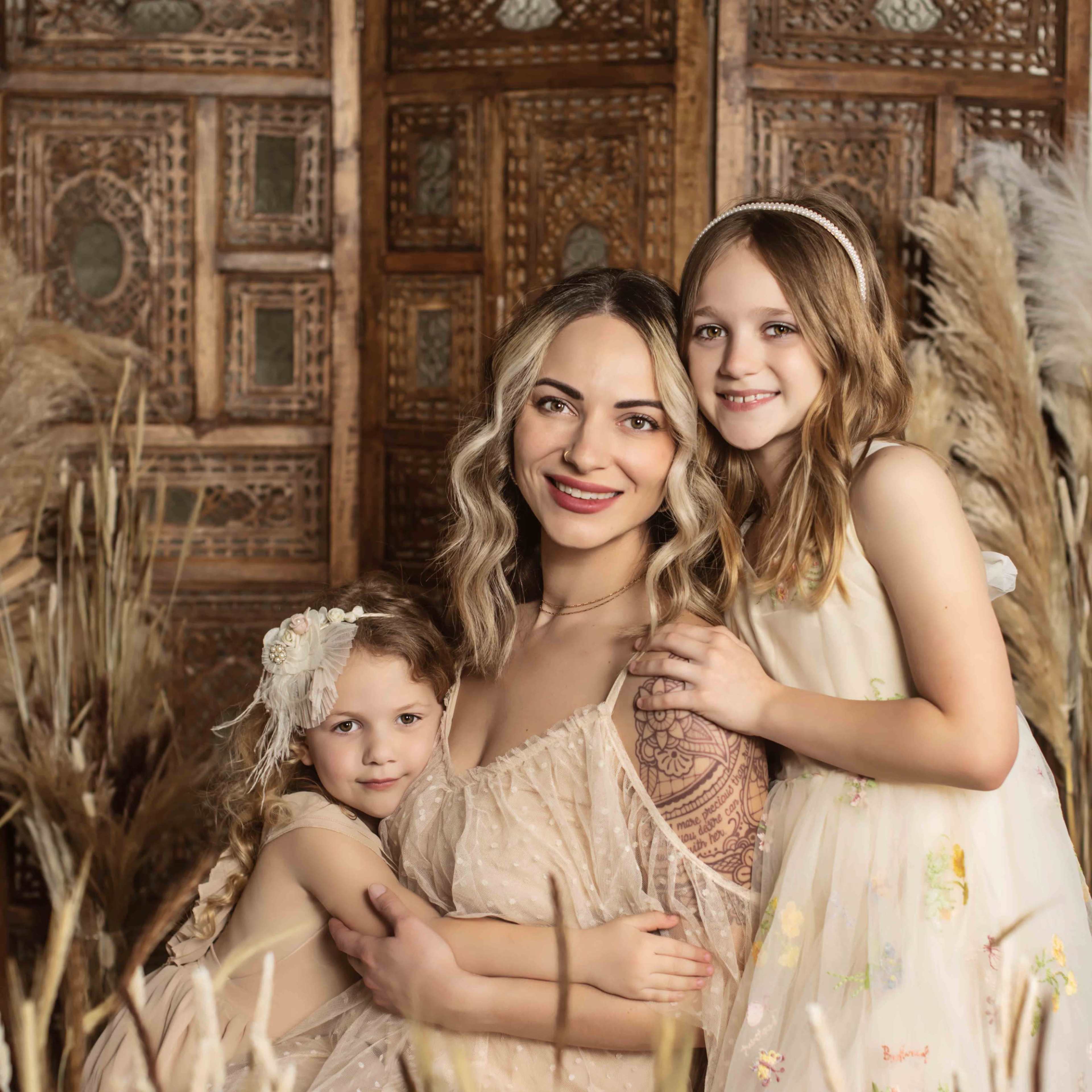 A woman poses with two young girls among tall grasses in a beautifully decorated indoor space.
