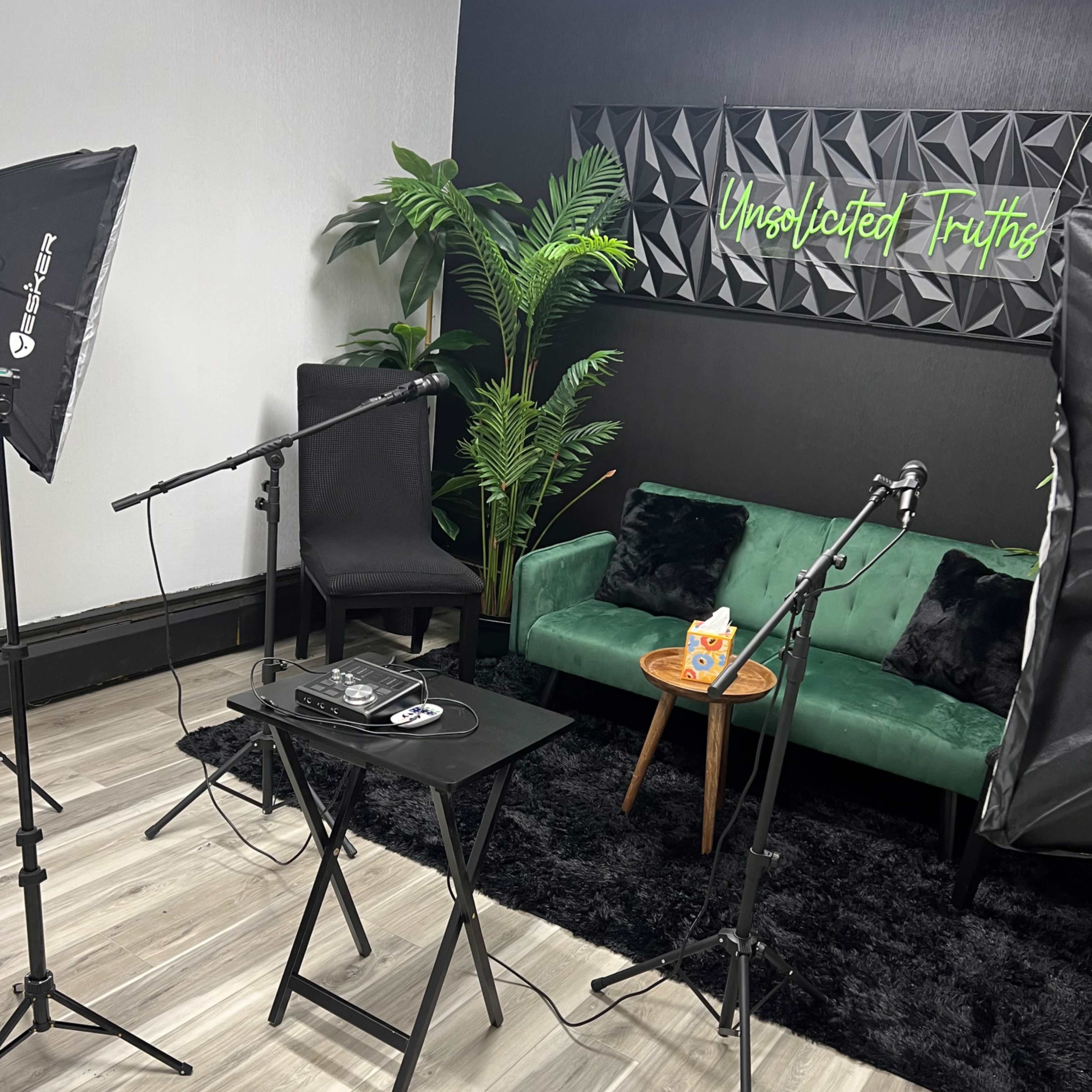 A video podcast setup featuring a green couch, a small wooden table with snacks, and professional lighting and microphones arranged in a studio space.