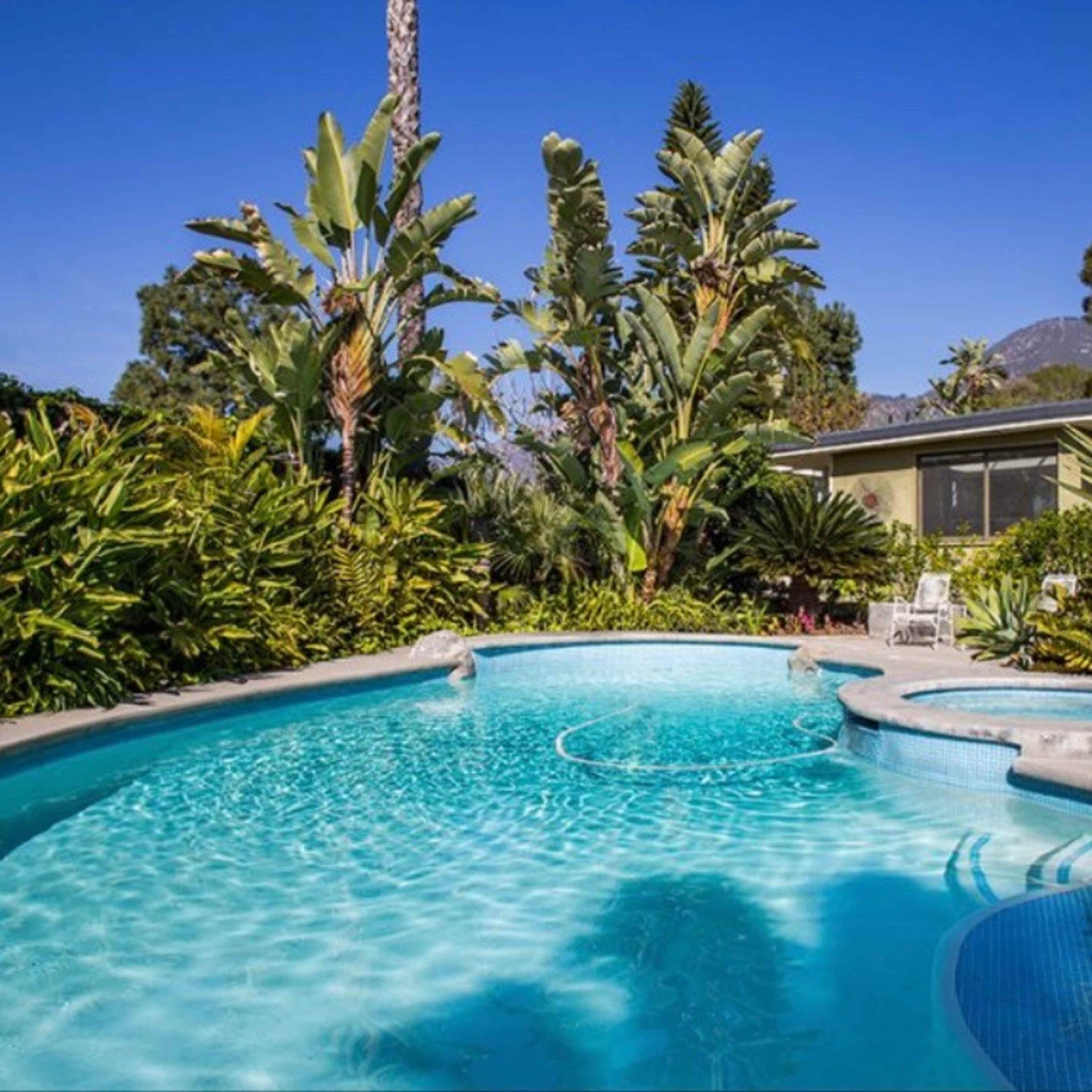 A swimming pool surrounded by lush tropical plants and trees, with a spa area integrated into the pool design.
