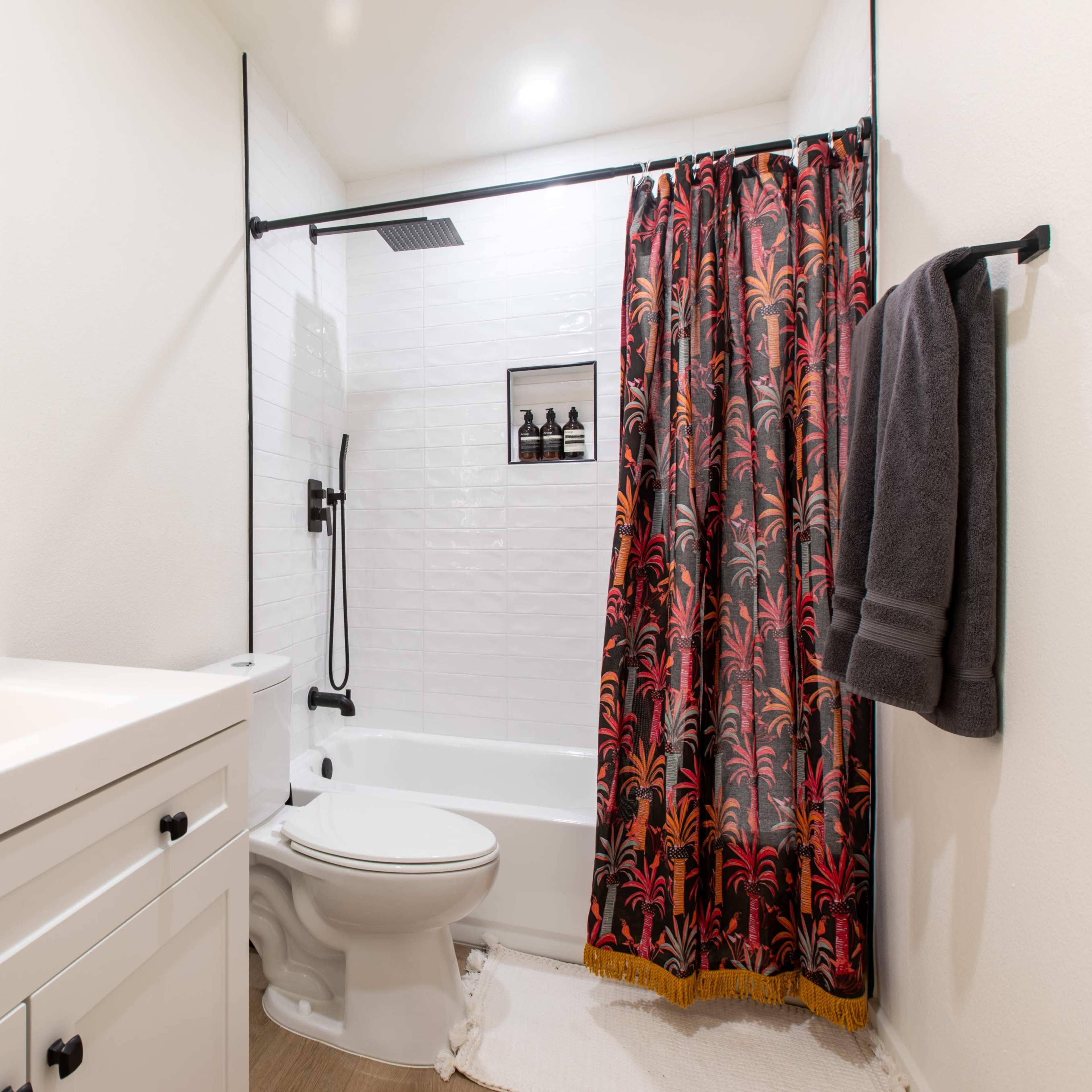 A modern bathroom featuring a bathtub with a shower, a bright mirror, and dark patterned curtains.