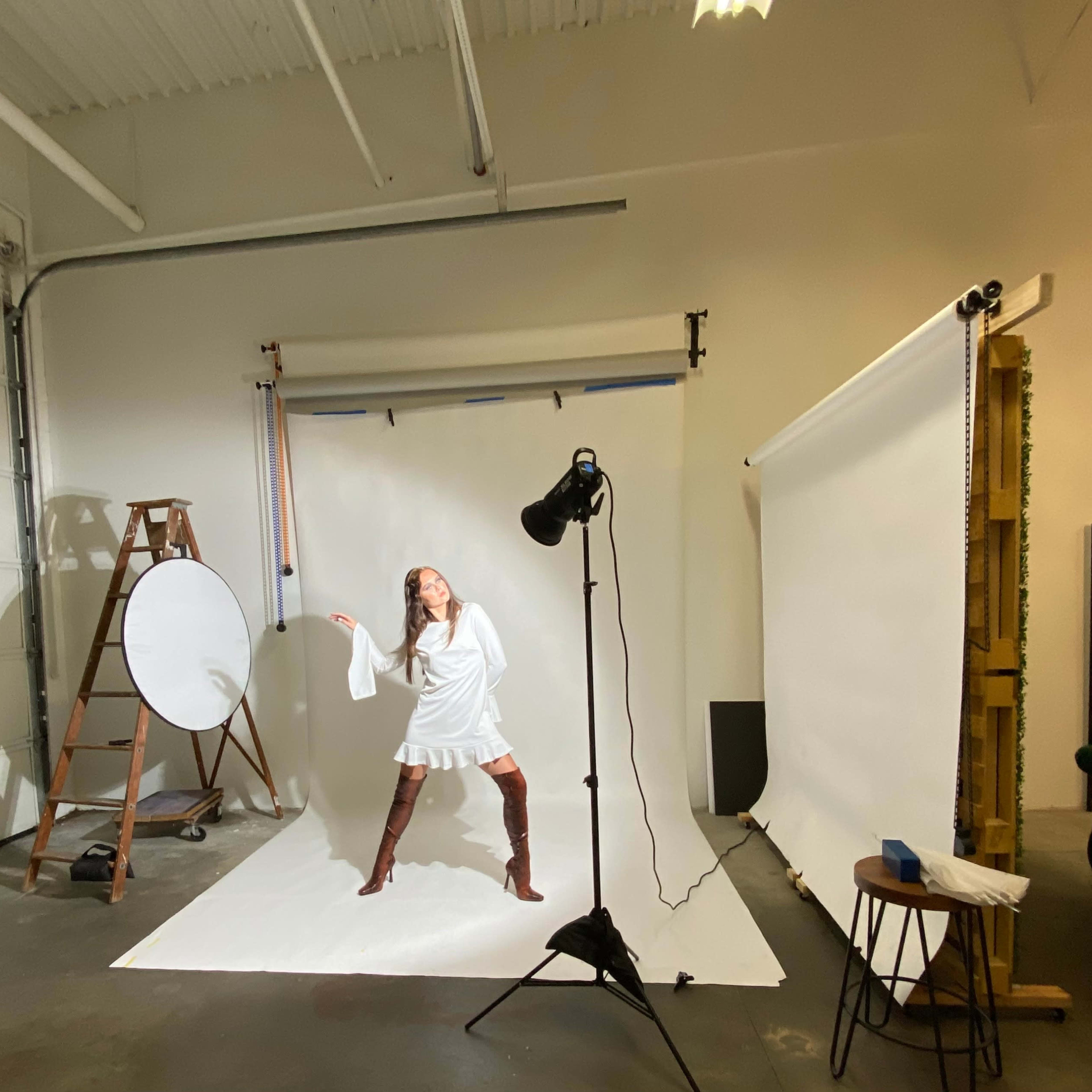 A model poses on a white backdrop in a photography studio equipped with various lighting and props.