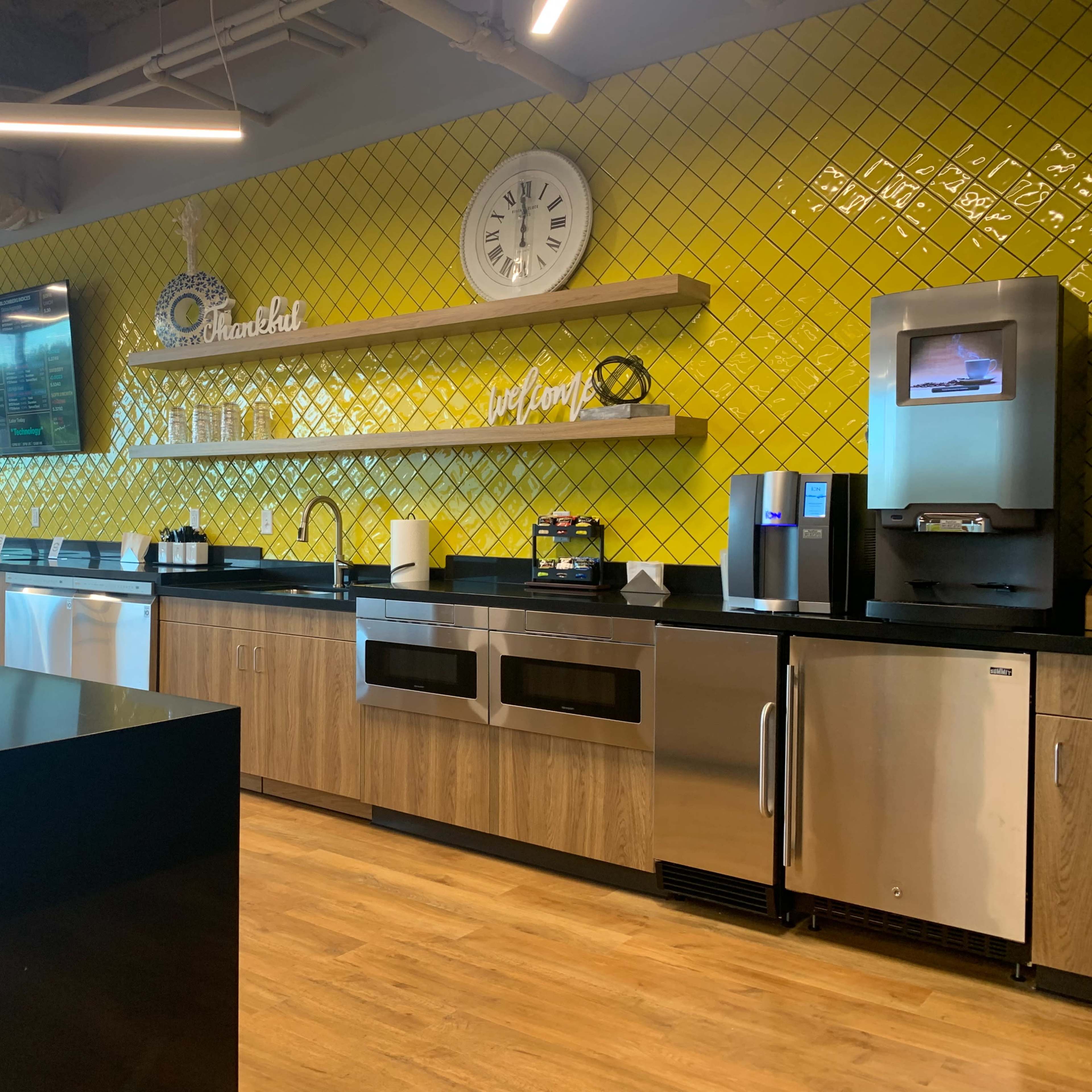 A modern kitchen area with yellow tiled walls, stainless steel appliances, and wooden cabinetry.