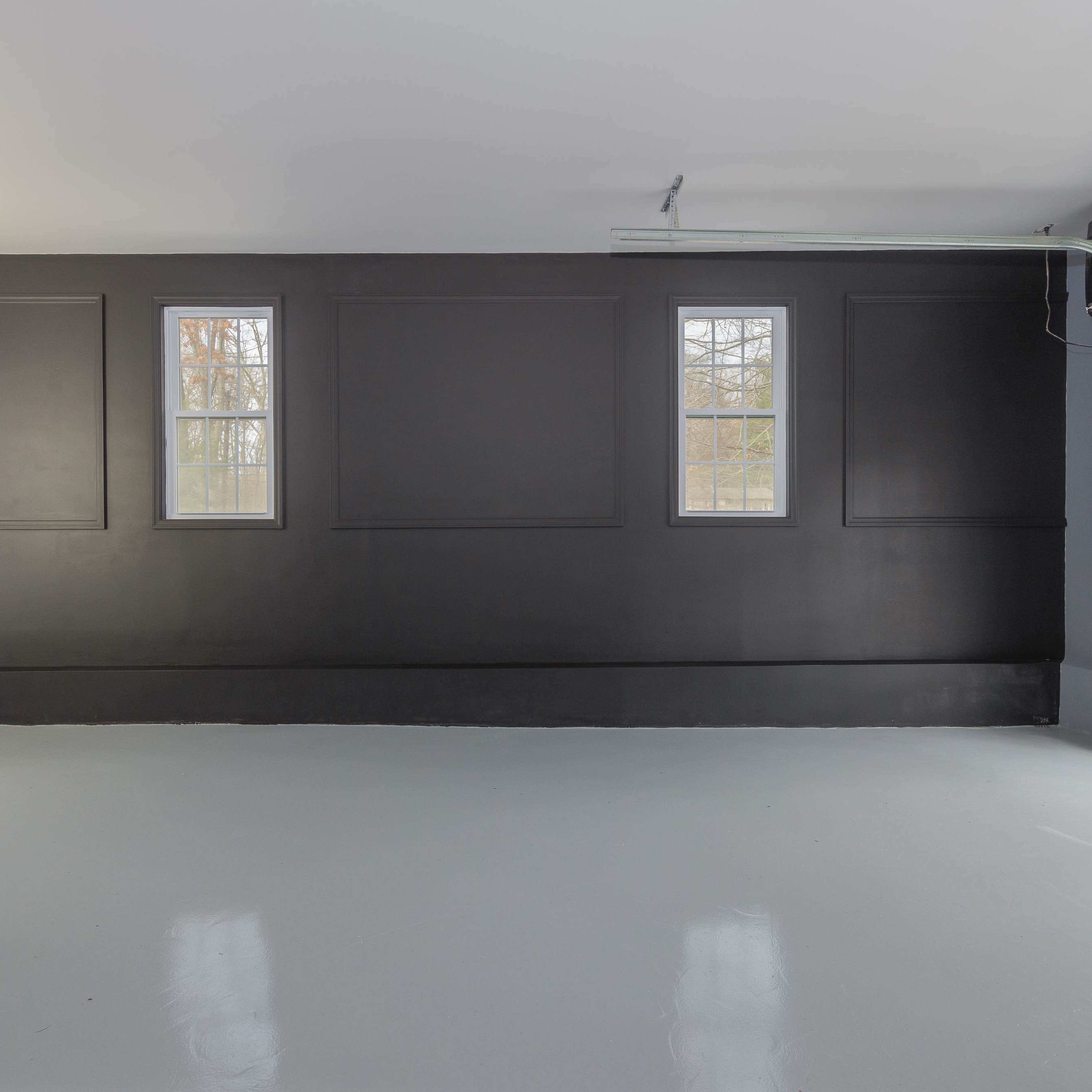 A spacious garage with a polished floor, black accent wall, two windows, and a roll-up garage door.